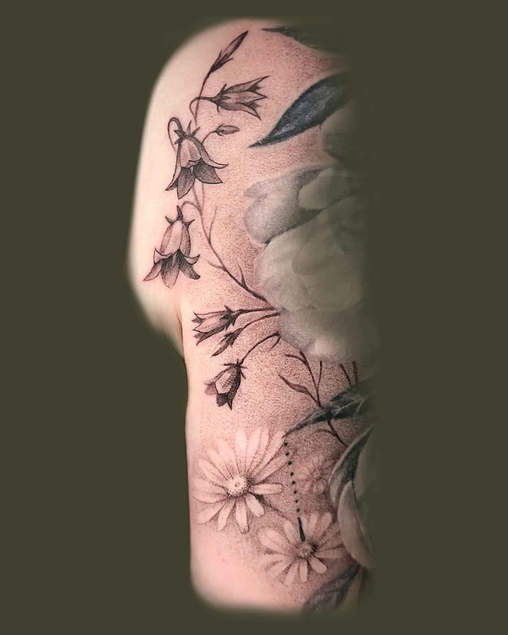 Kuva kädestä, jossa on tatuoitu kukkia, voikukkia ja kissankelloja.