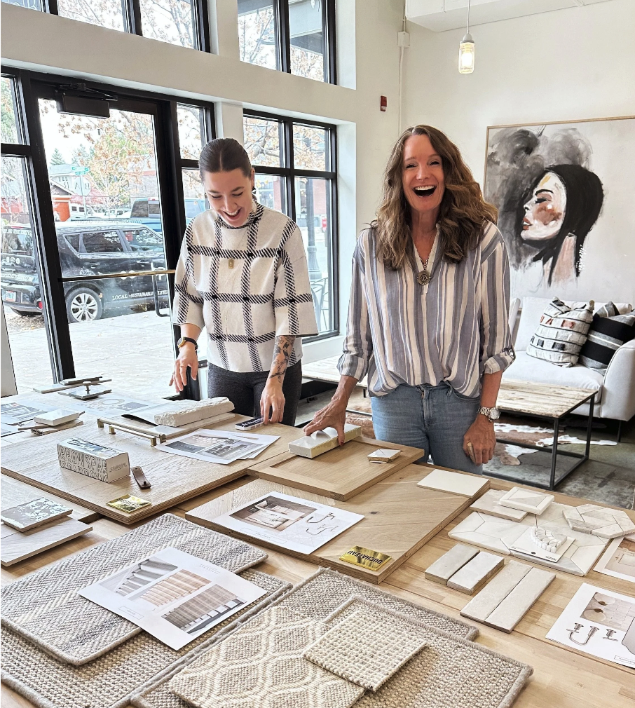 Anne Mastalir, founder of Design Bar Interiors Bend and Skyhouse Collective, laughing with a team member and looking over interior design mockups and fabric/textile samples