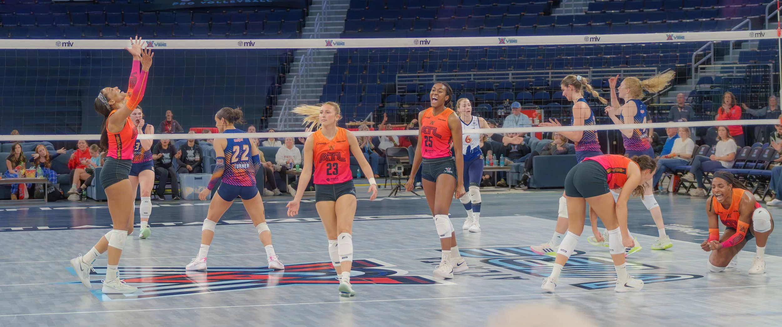 Women volleyball players celebrating during a game in an indoor arena with spectators in the background.