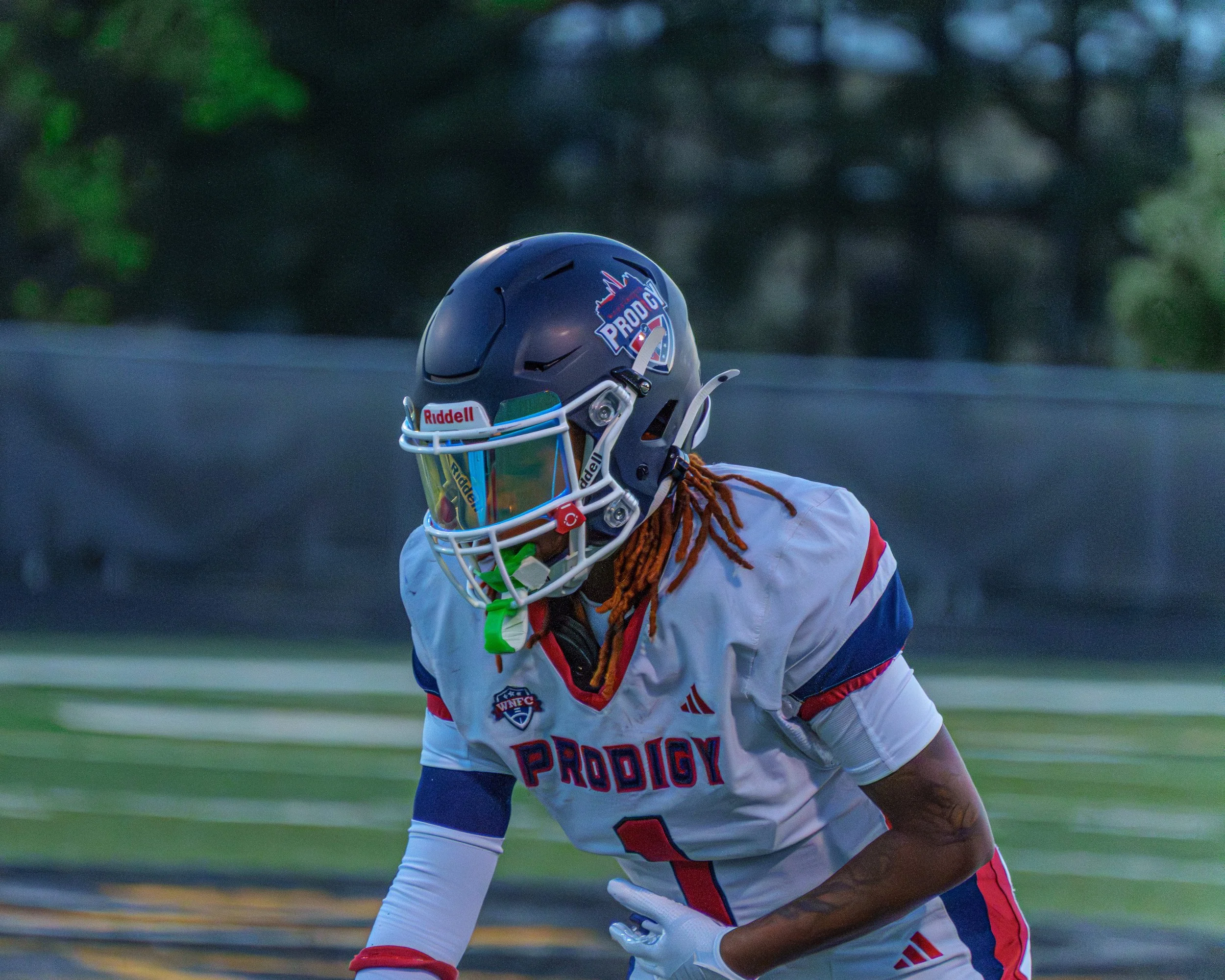 American football player wearing a white, blue, and red uniform with the number 1 and a black helmet with a visor, on a football field during a game.