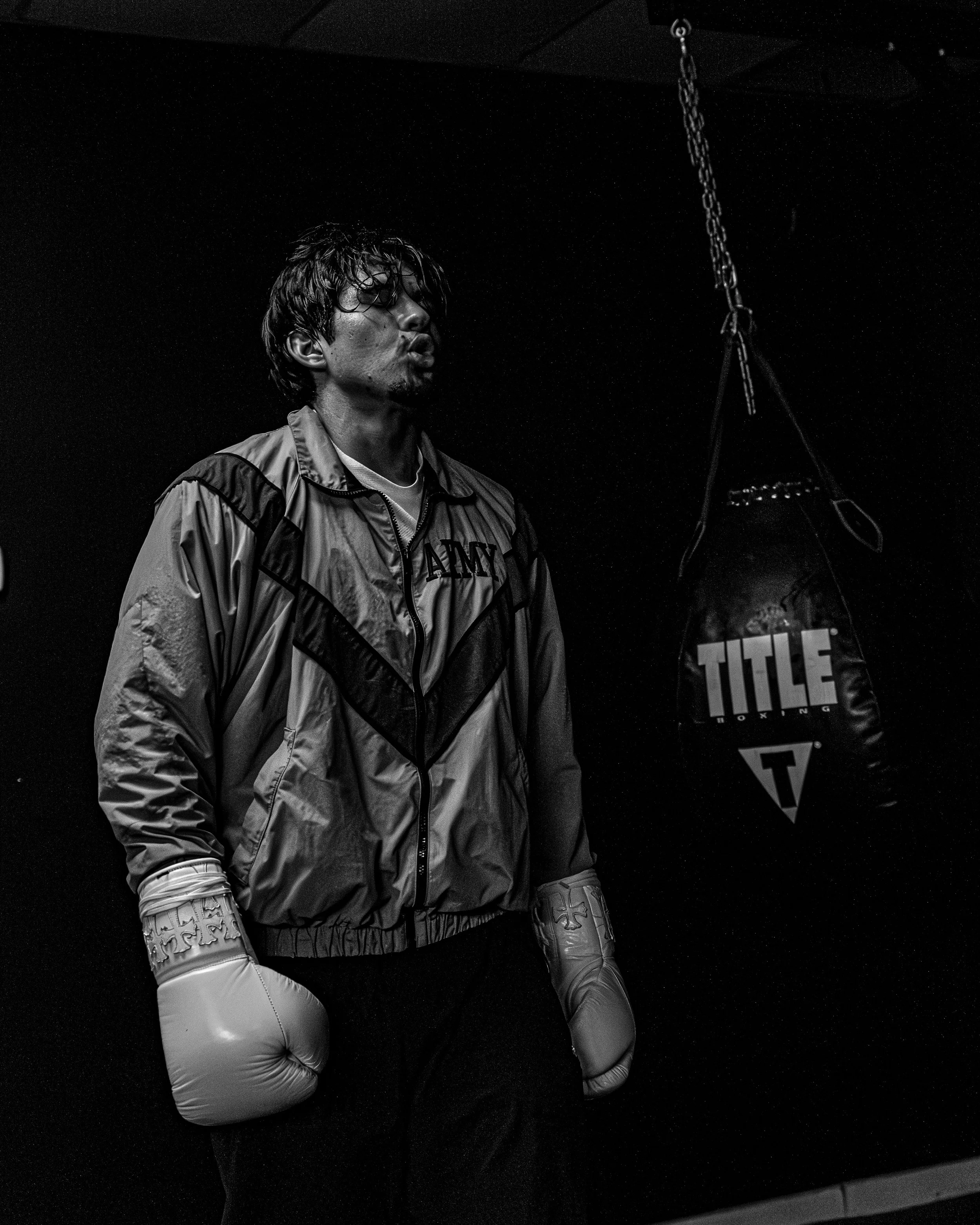 A young boxer wearing boxing gloves and athletic clothing, standing in a boxing gym next to a punching bag.