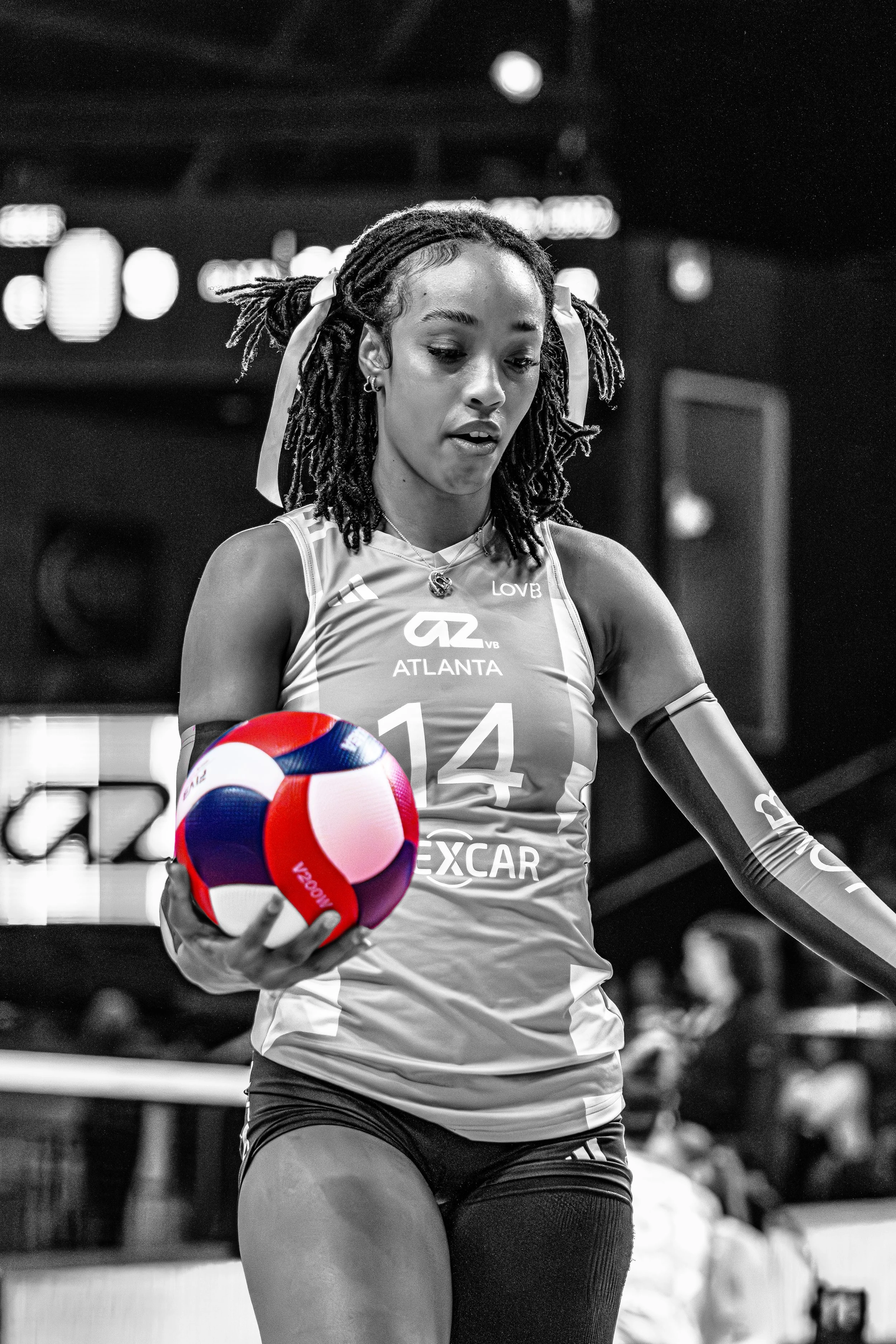 A female volleyball player in a jersey with the number 14, holding a multicolored volleyball during a match.