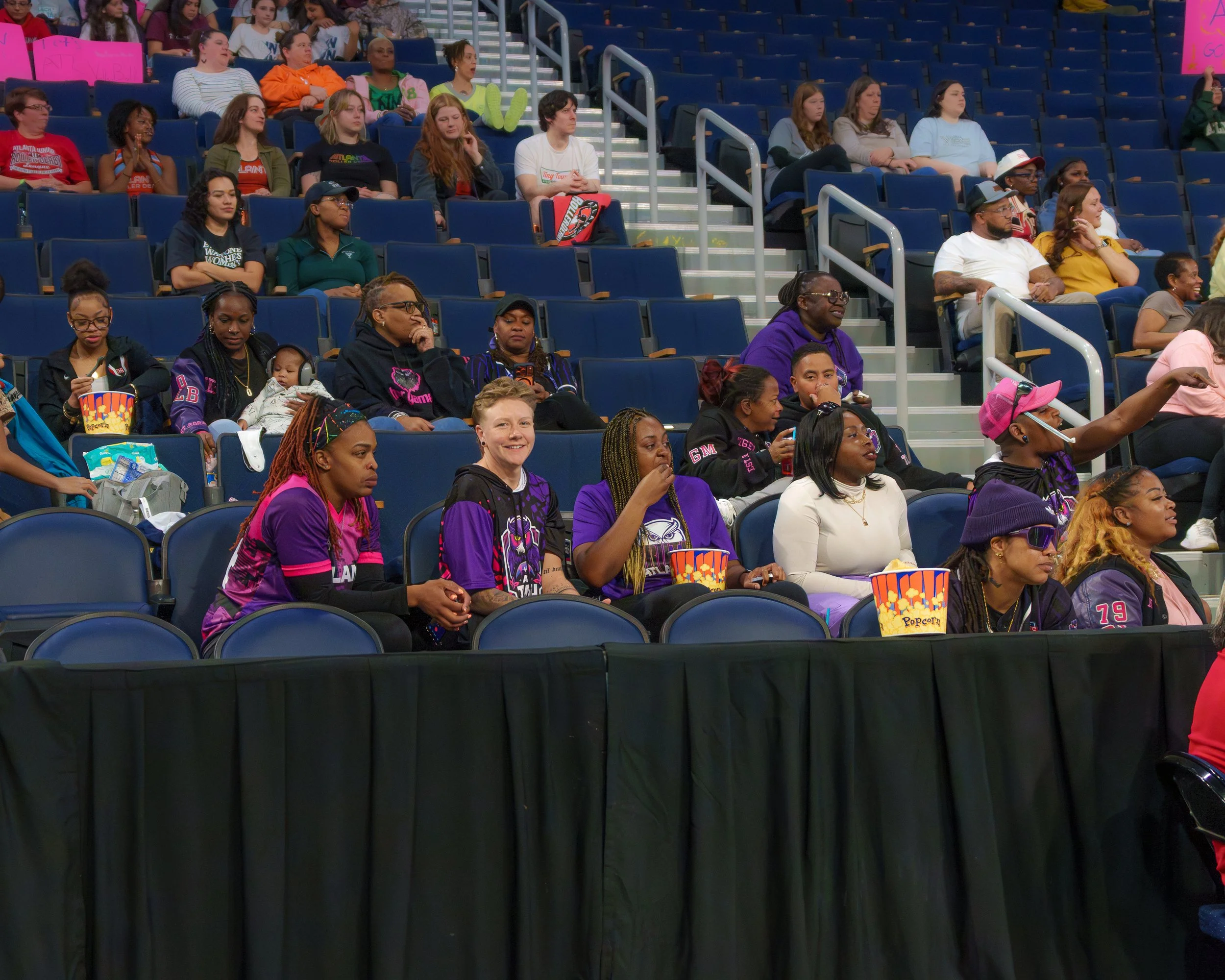 Audience seated in stadium seats, some with popcorn, watching an event.