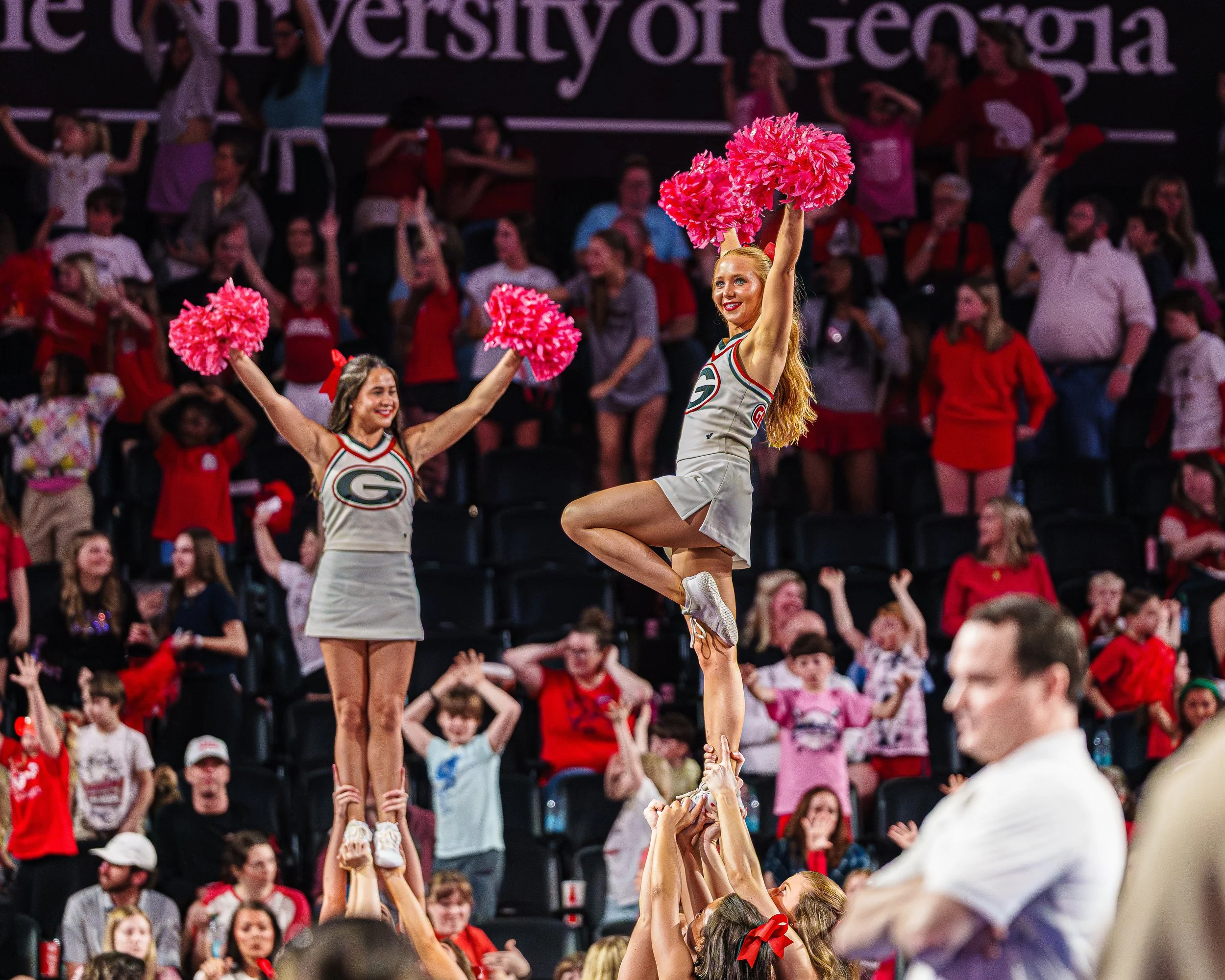 Cheerleaders performing a stunt during a sports event with crowd in background