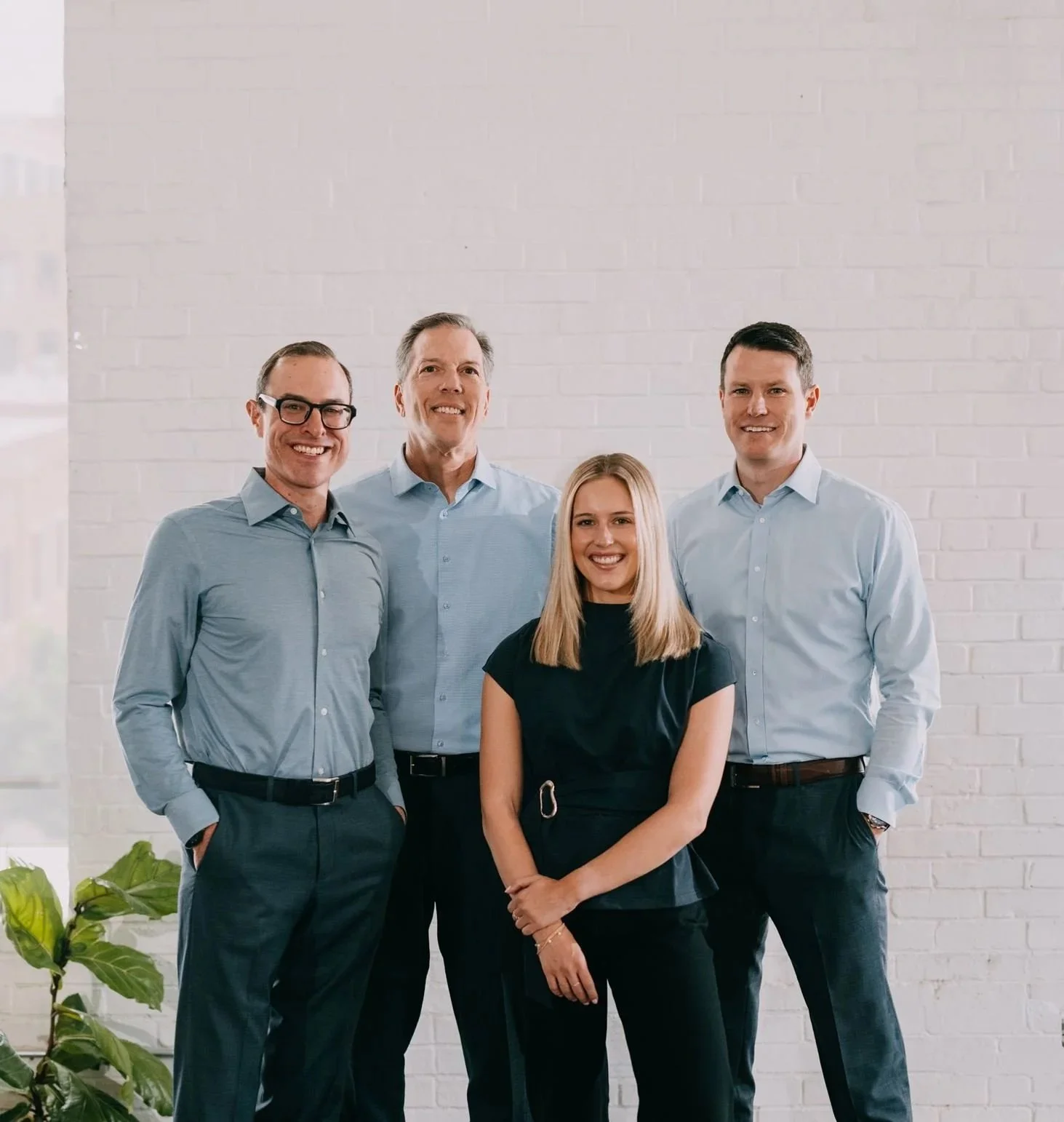 Five professional people standing together against a white brick wall, smiling at the camera.
