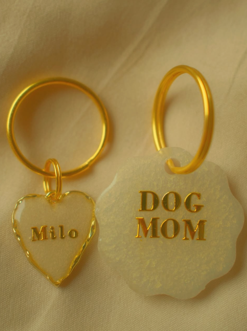 Zwei Schlüsselringe, einer mit einem Herzanhänger mit der Aufschrift 'Milo' und einer mit einem runden Anhänger mit der Aufschrift 'DOG MOM'
