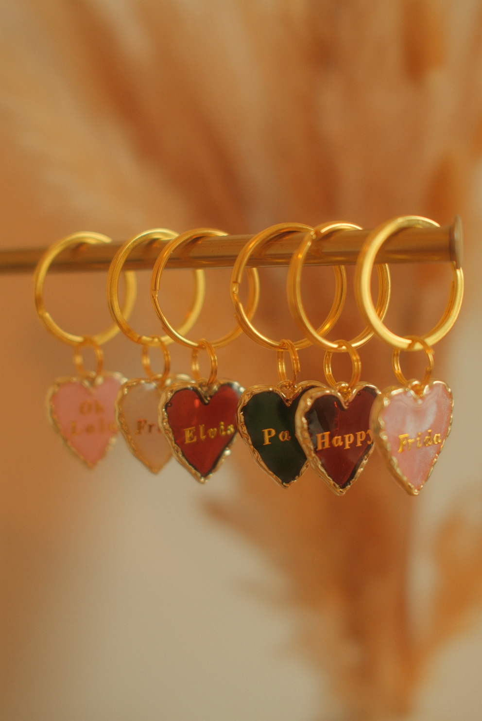 Goldene Ohrringe mit herzförmigen Anhängern, die die Namen verschiedener Personen tragen, hängen an einem goldenen Haken.