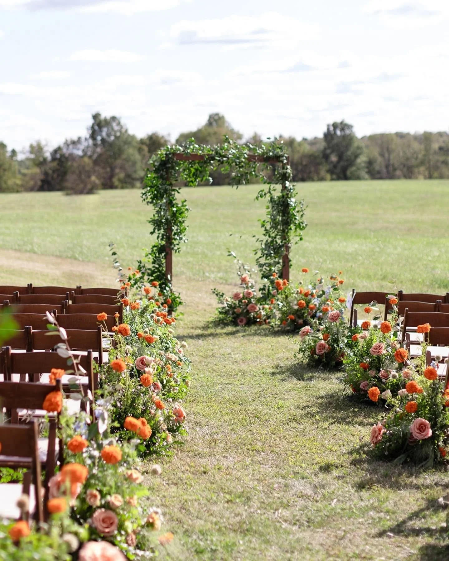 Outdoor wedding ceremony setup with flowered aisle and arch in a grassy field