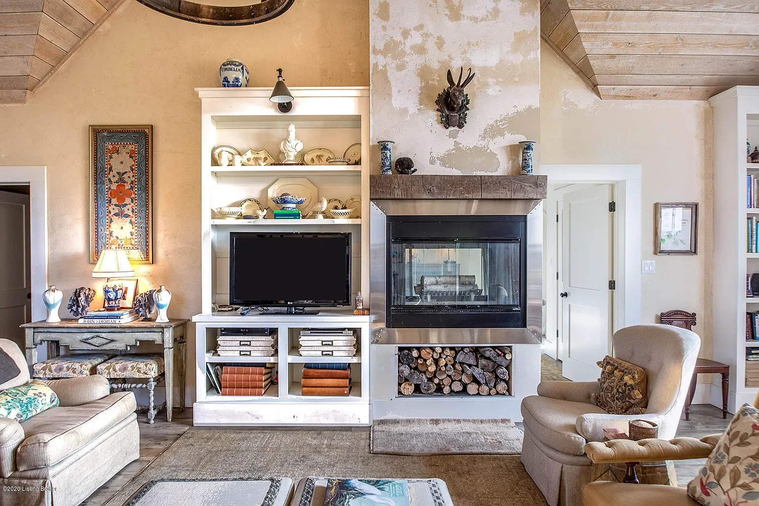 Living room with fireplace, television, and built-in shelves, with furniture including armchairs and a coffee table.