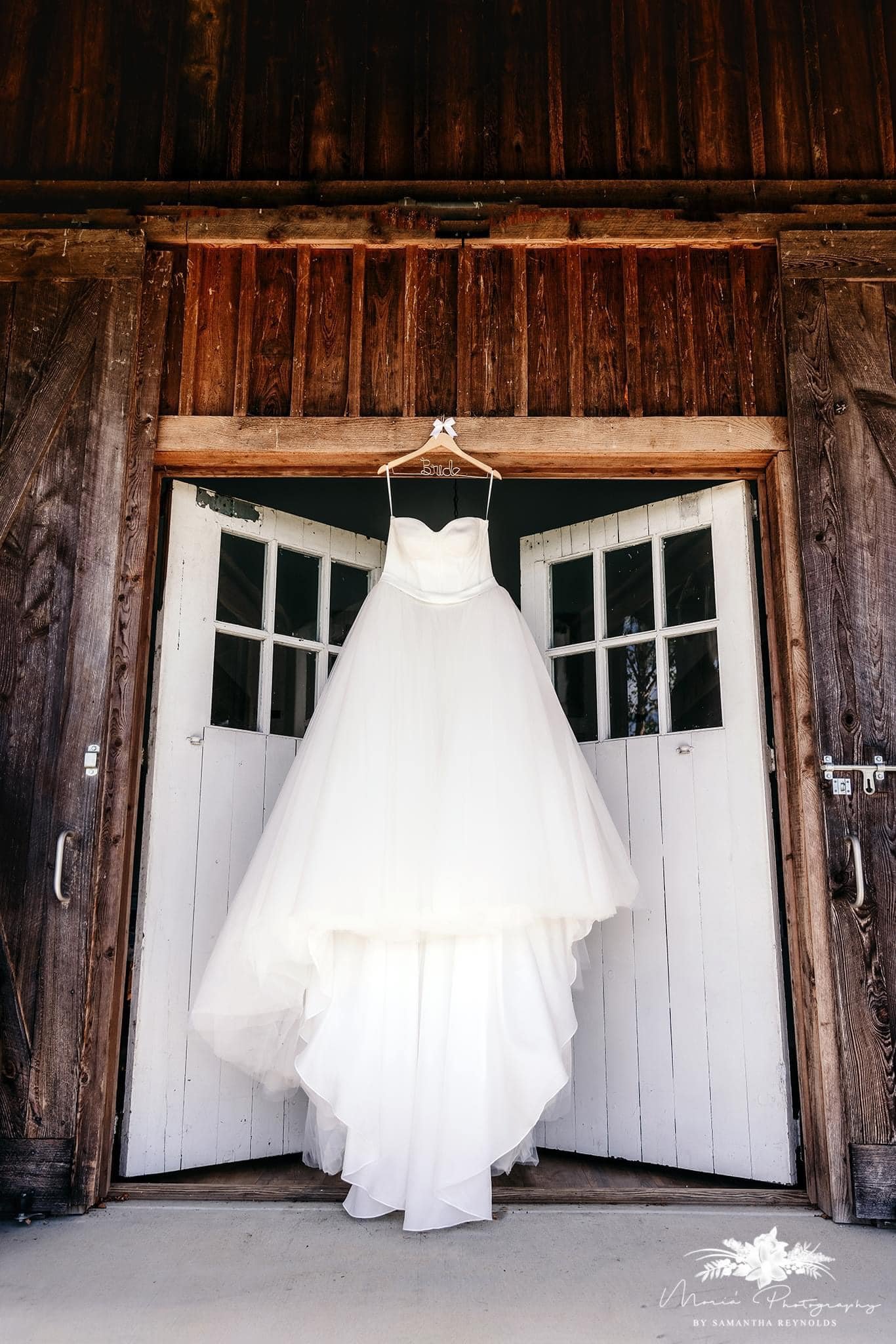 White wedding dress hanging on a wooden door frame outside a rustic barn.