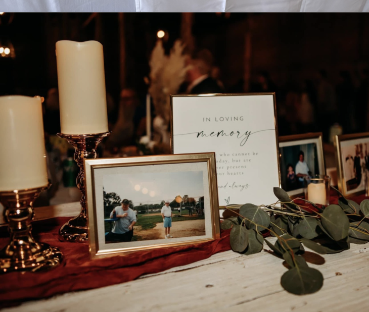 A memorial display table with framed photos, candles, and a sign that reads 'In Loving Memory' at an indoor event.