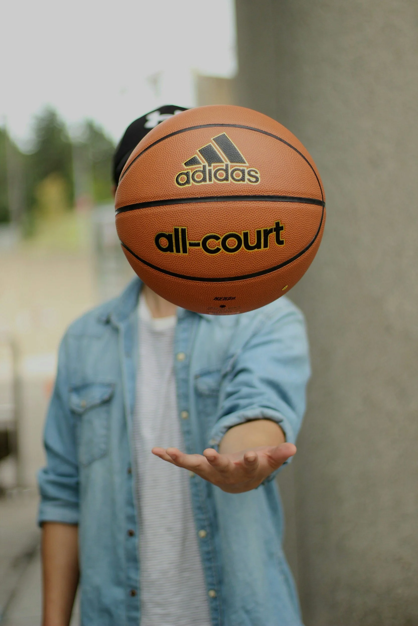 Person in a denim jacket and striped shirt holding out their hand with a basketball in front of their face.