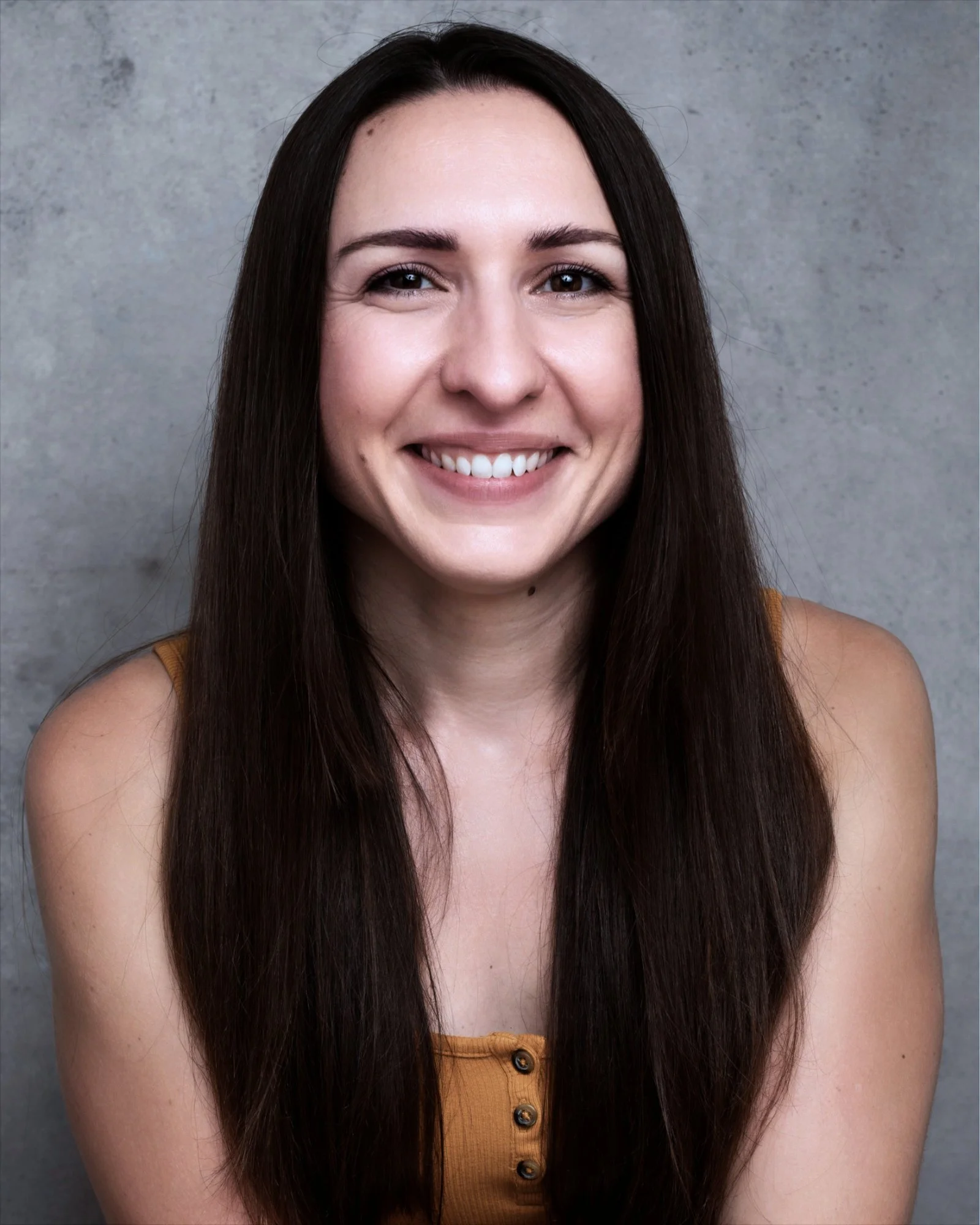A woman with long dark hair smiling in front of a plain gray background.