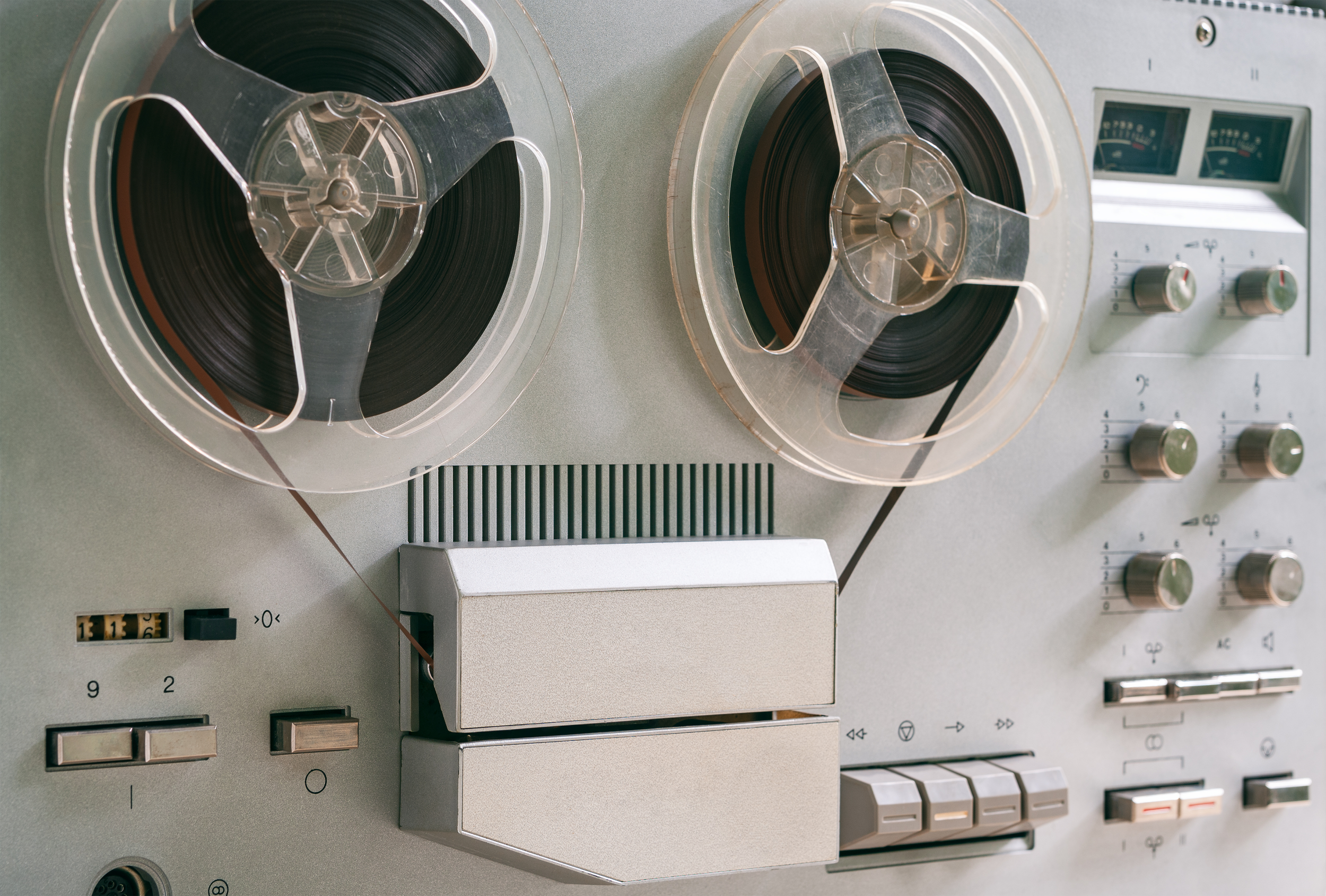 A vintage reel-to-reel tape recorder with two large spools of magnetic tape, control knobs, switches, and display meters.