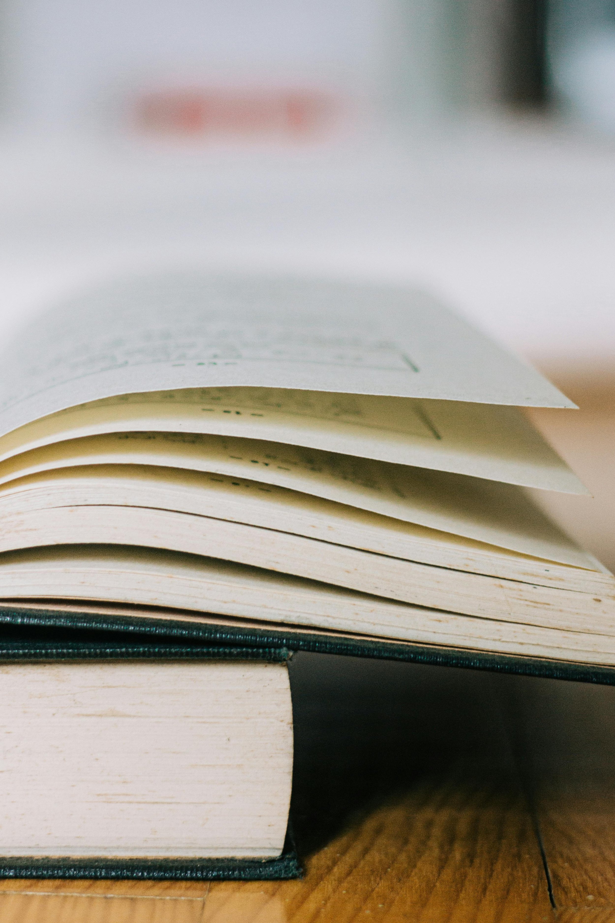 Close-up of an open book lying flat on a wooden surface with pages partially turned.