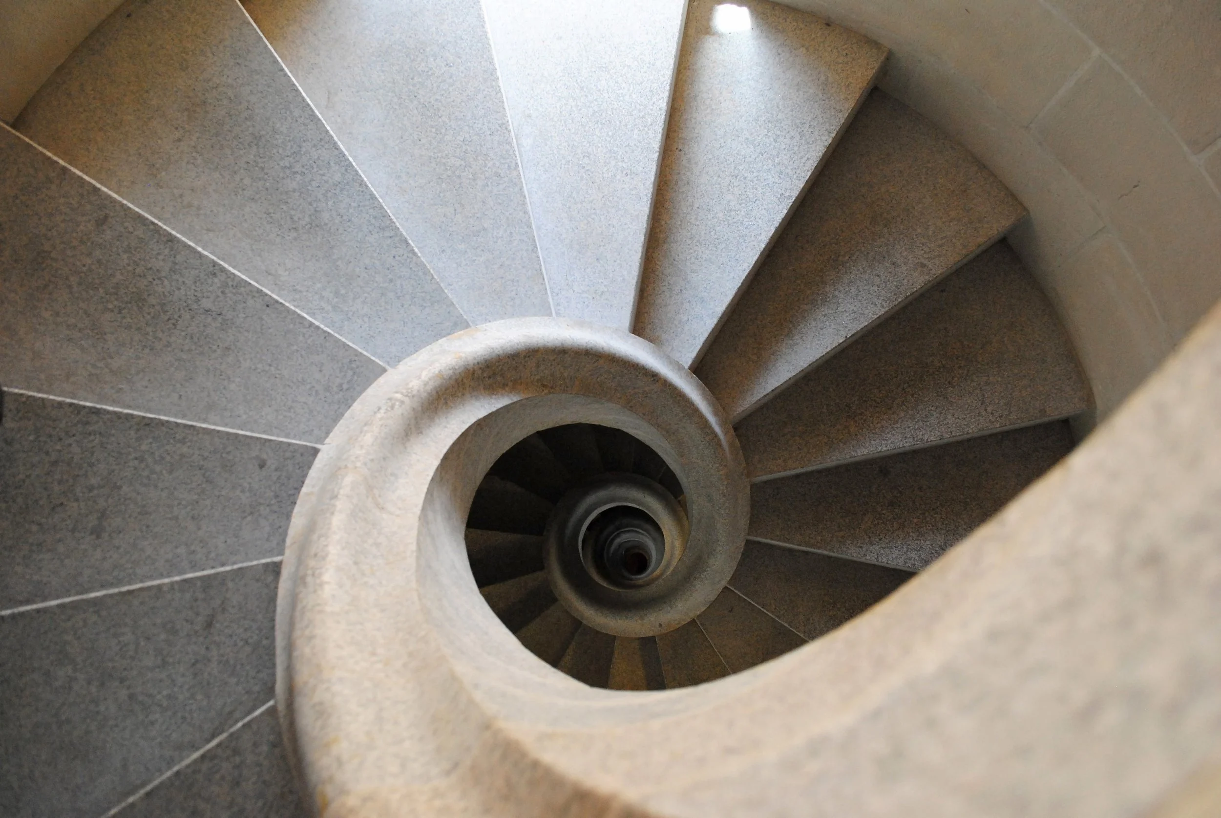 Top view of a spiral staircase with grey stone steps and beige outer wall.