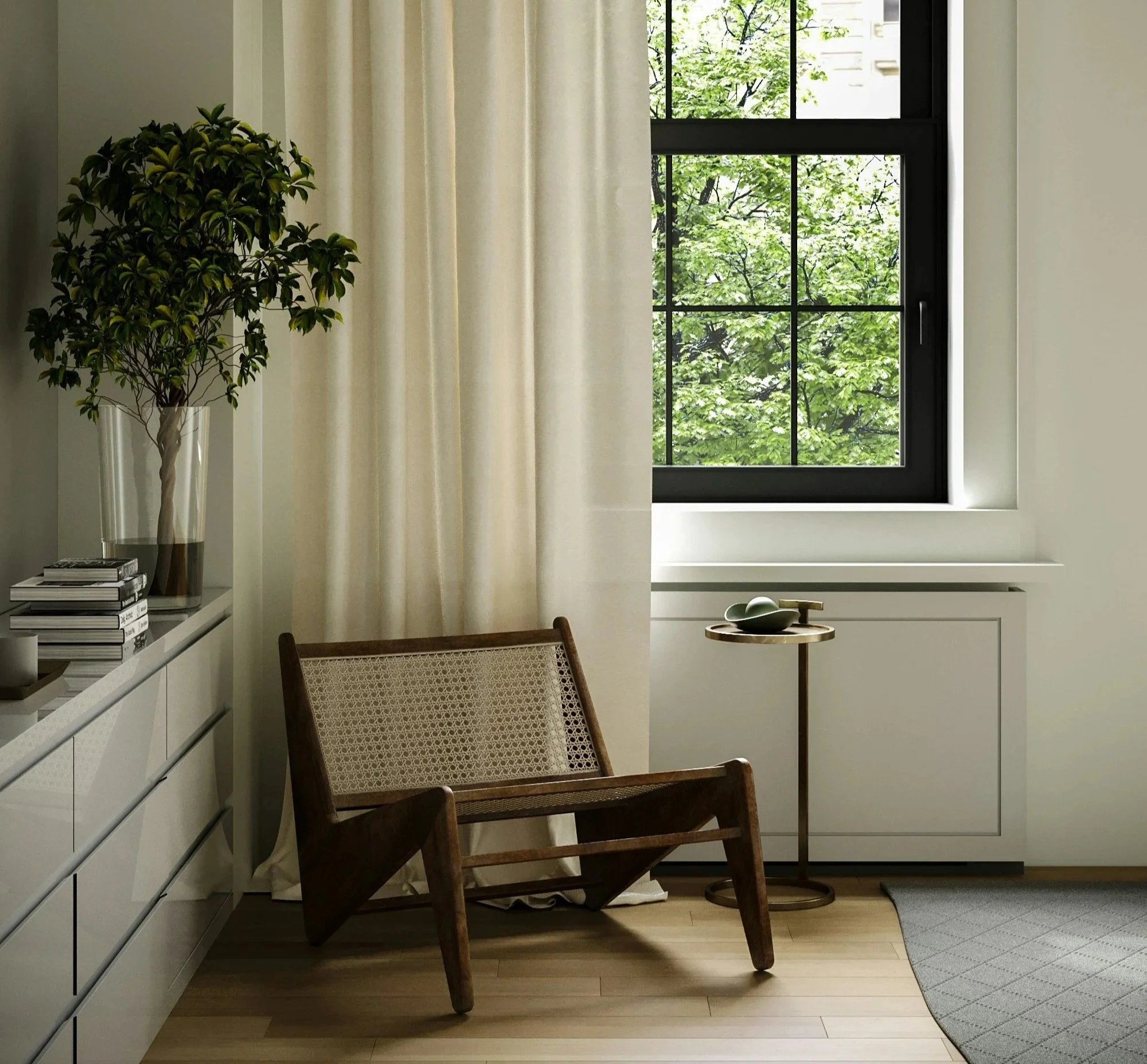 A cozy corner of a room with a large window showing green trees outside. There is a wooden chair with a woven backrest, a small round side table with a bowl and a spoon, a potted green plant, and a stack of books next to a white larger cabinet. Cream-colored curtains hang partly open, and a gray rug is on the light wooden floor.