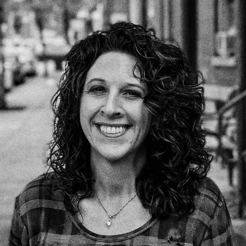 Black and white photo of a woman with curly hair smiling outdoors.