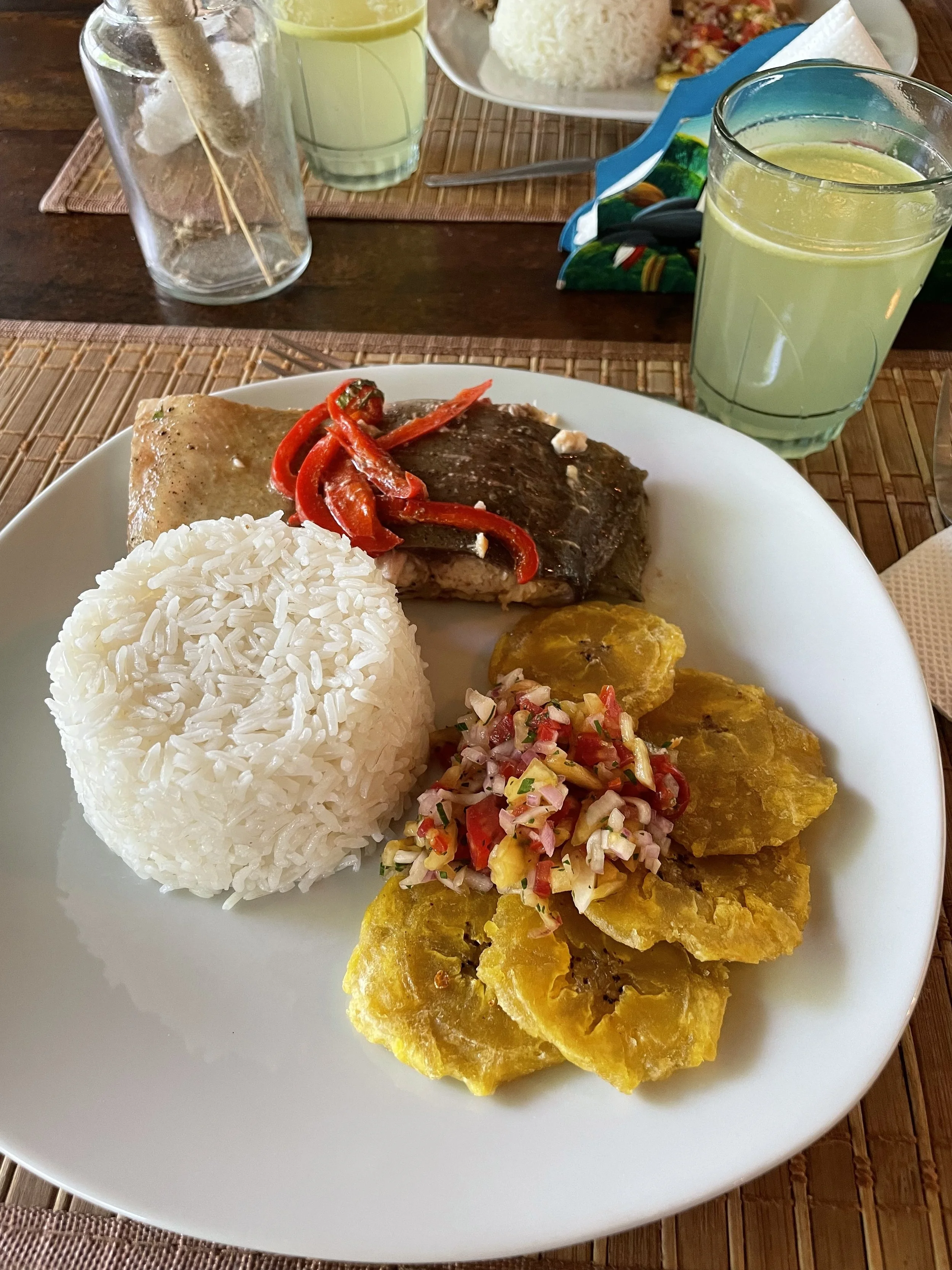 Plat typique africain avec riz blanc, poisson grillé avec poivrons rouges, plantains frits avec salsa à base d'oignons, tomates et piment, et deux boissons vertes
