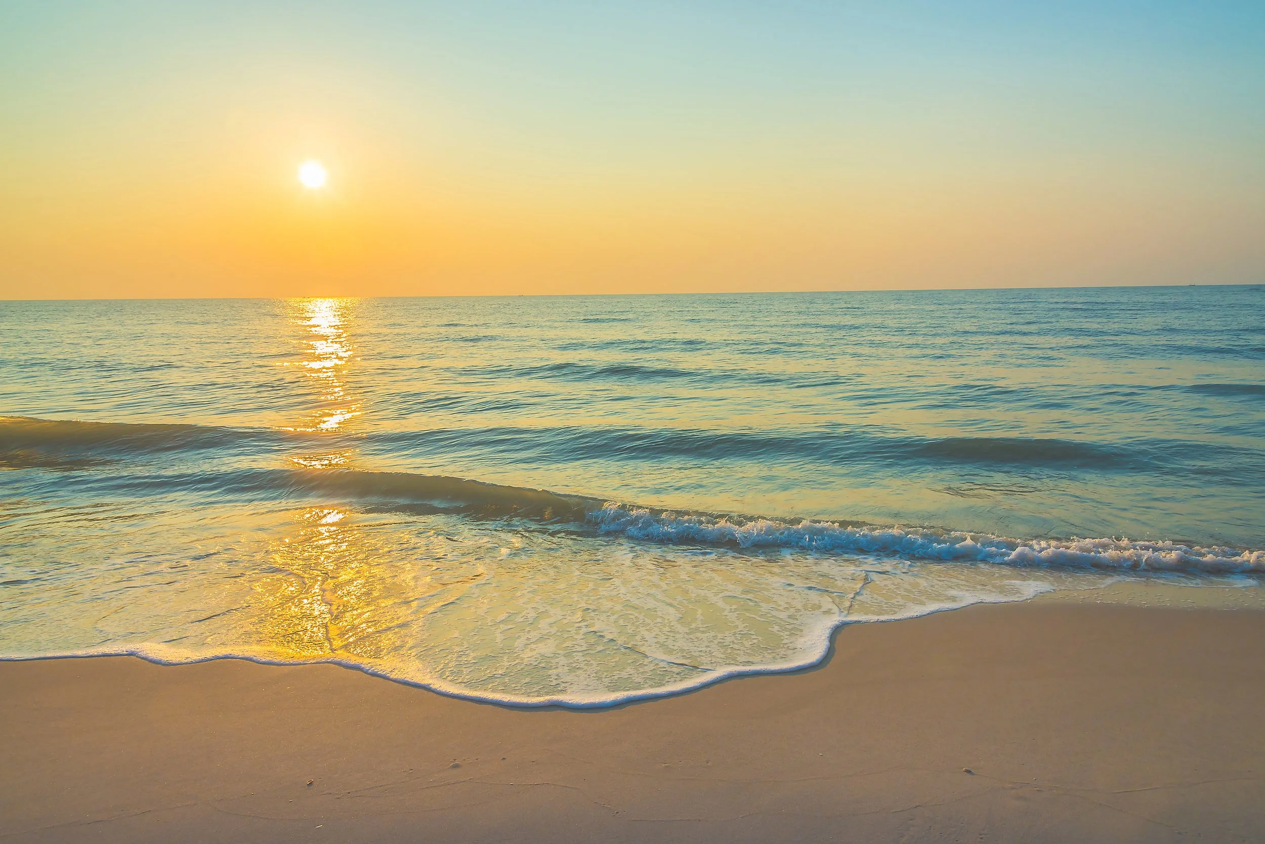 Coucher de soleil sur une plage avec mer calme et sable doré.