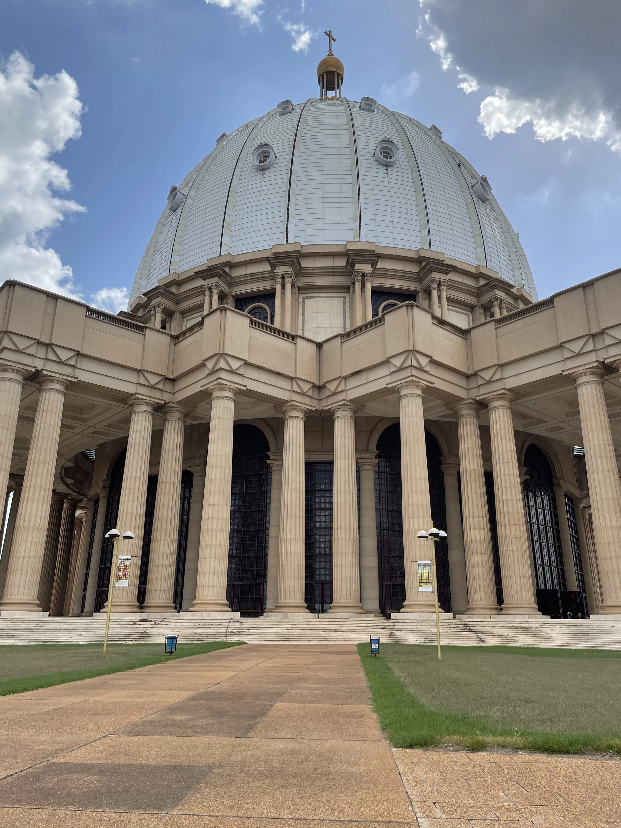 Vue du dôme d'une basilique ou église avec colonnes et escalier, ciel partiellement nuageux.