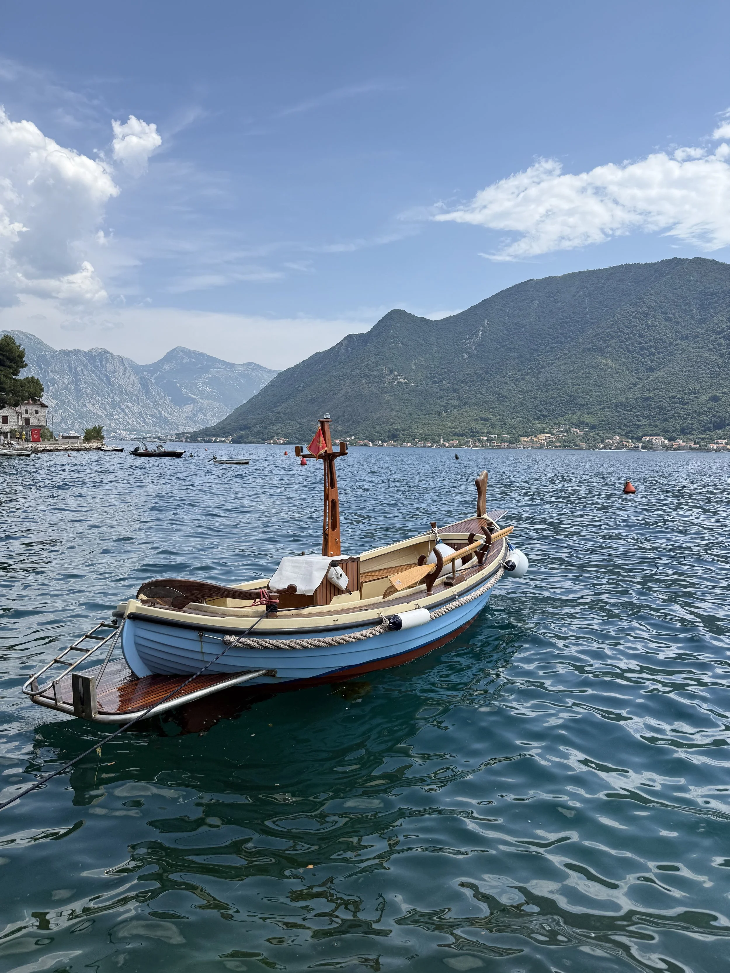 Bateau en bois traditionnel flottant sur un lac entouré de montagnes verdoyantes sous un ciel partiellement nuageux.