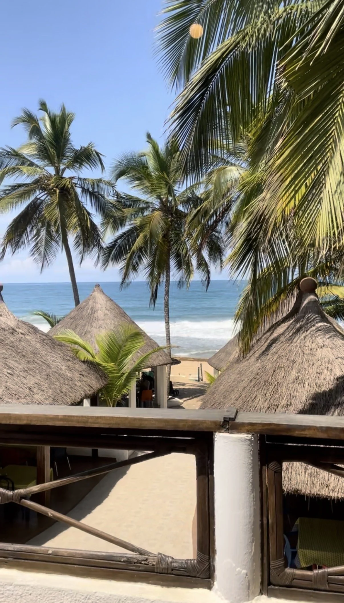 Plage tropicale avec palmiers, cabanes en chaume, et mer bleue sous un ciel ensoleillé.