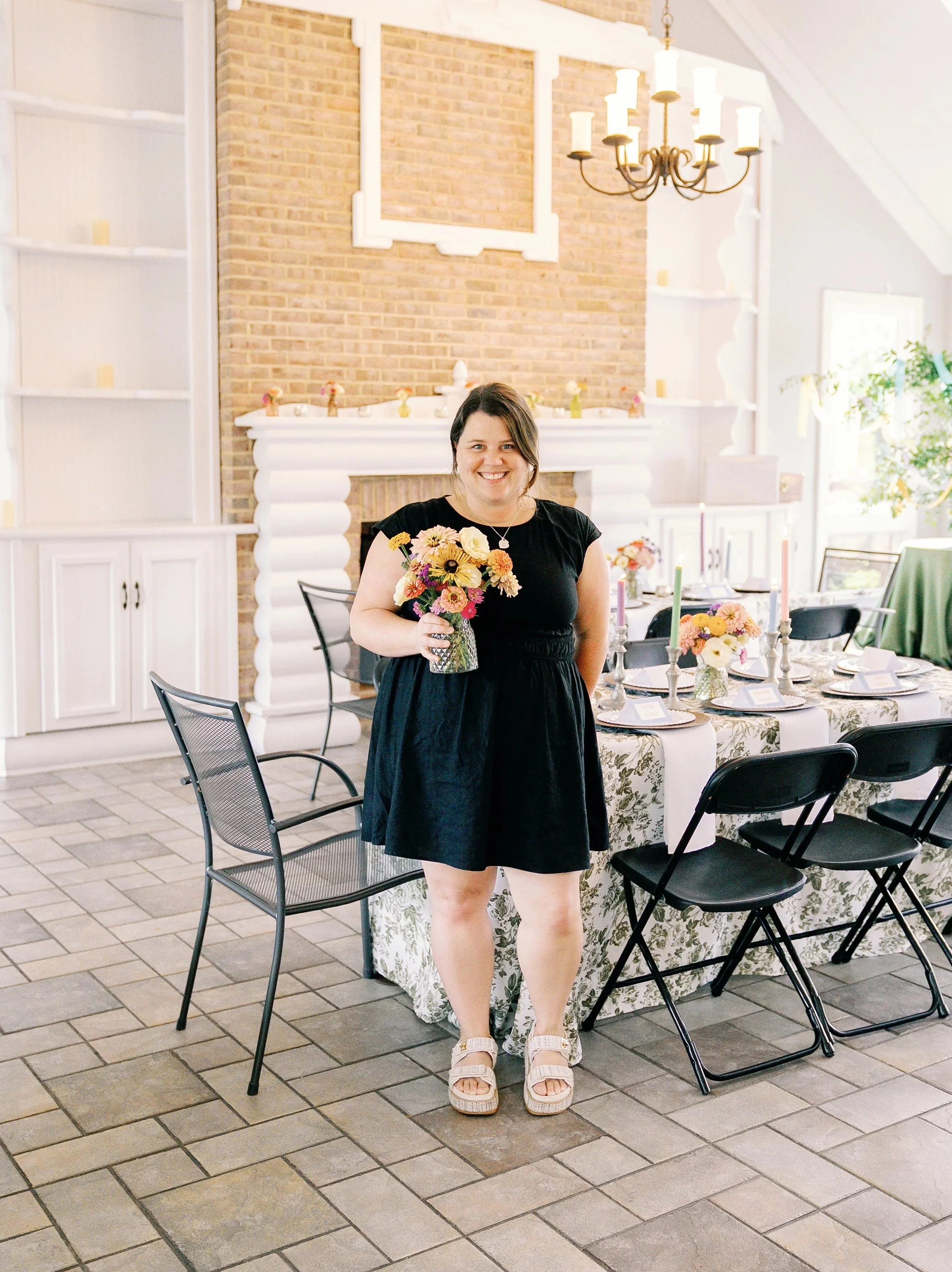 Fleurish florist holding a colorful wildflower bouquet at a styled bridal shower table setting with floral linens and candlesticks