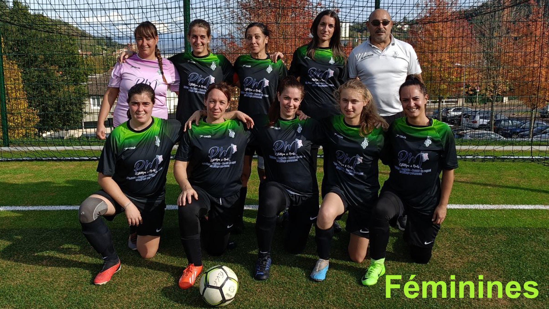 Équipe féminine de football en uniforme noir et vert, photo prise sur un terrain de sport avec un but en fond, arbres et voitures en arrière-plan, mot 'Féminines' en bas à droite.