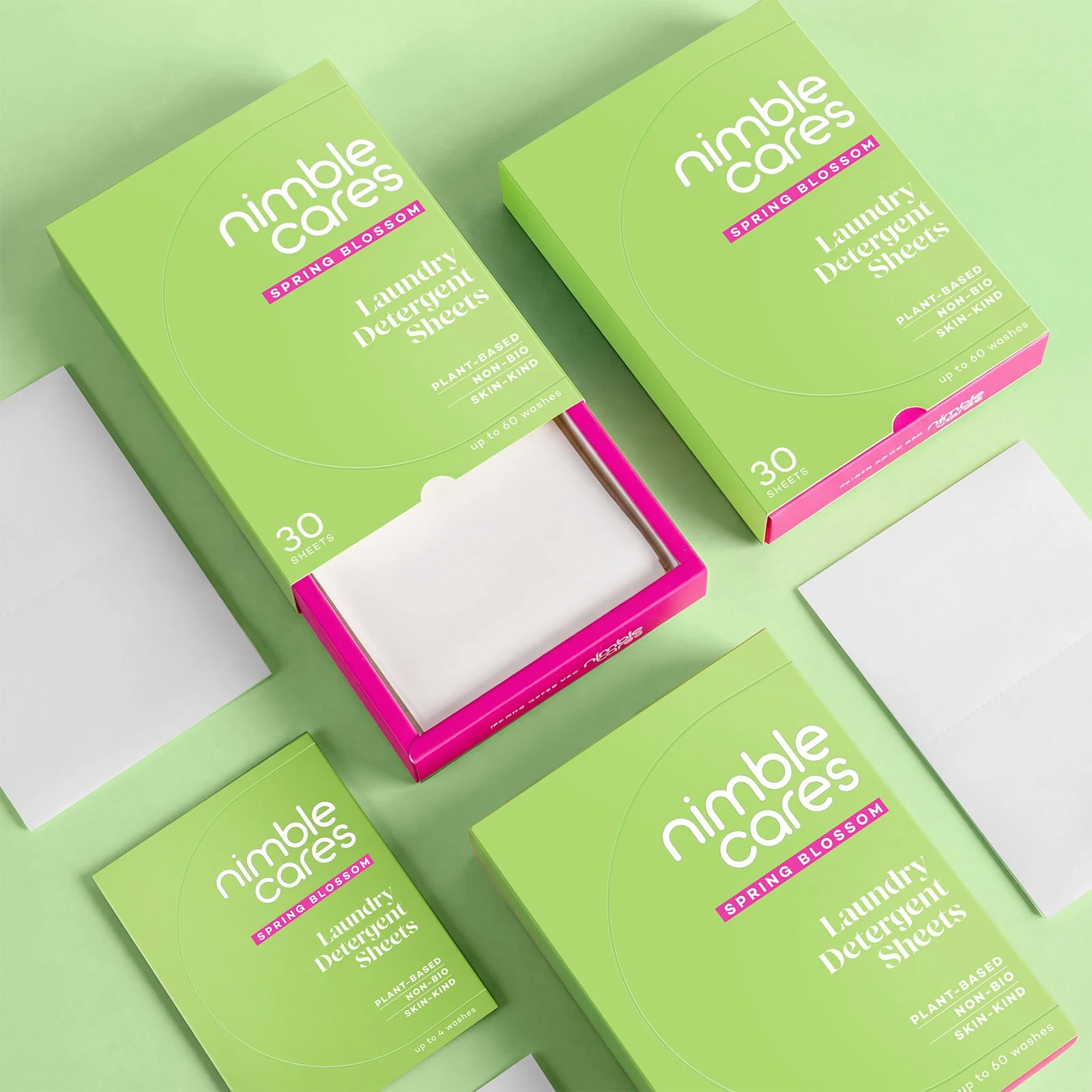 Three boxes of Nimble Cares Spring Blossom laundry detergent sheets with some sheets removed from the packages, on a green background.