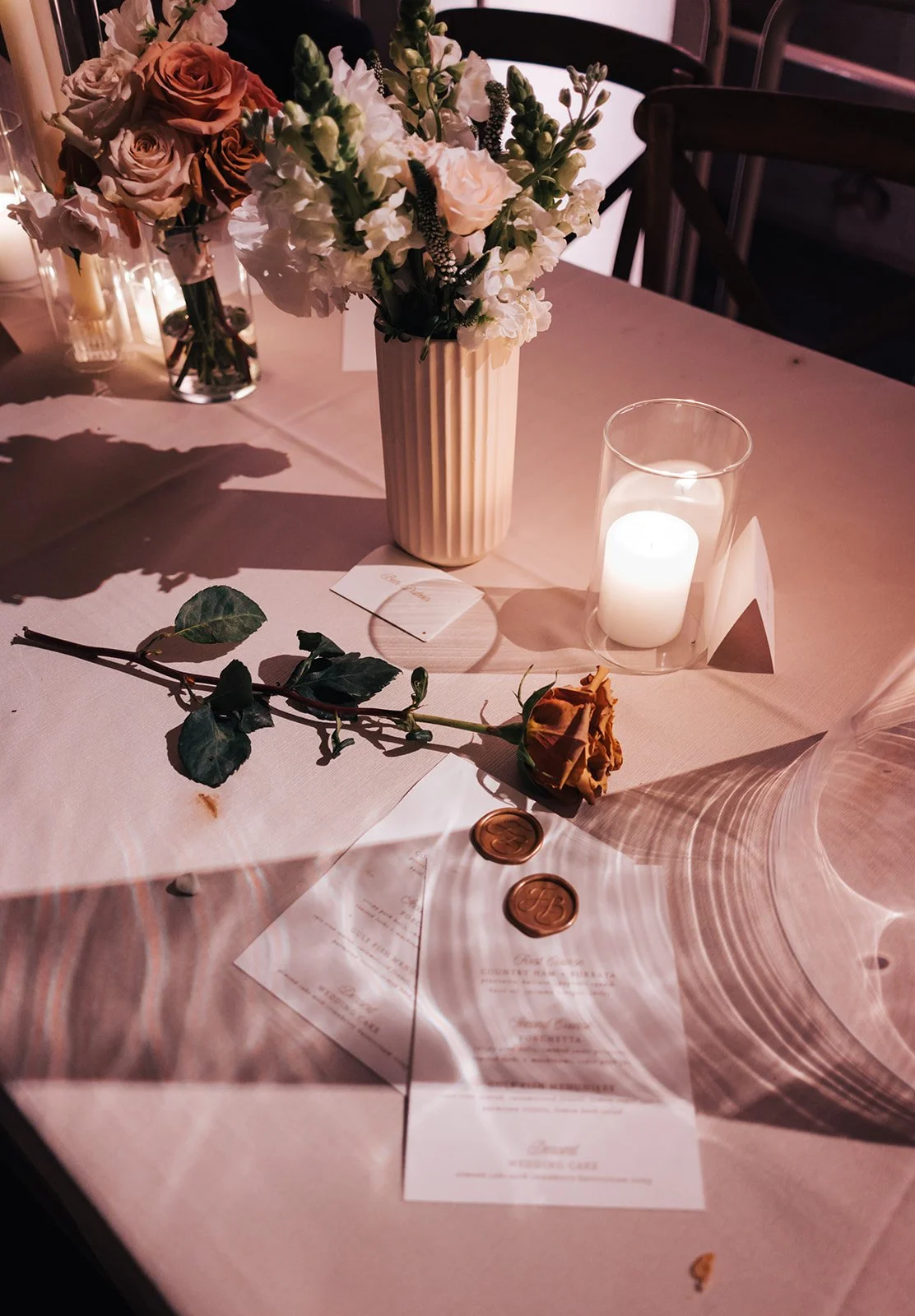 A table set for a wedding or formal event with floral arrangements, a lit candle, and a rose.