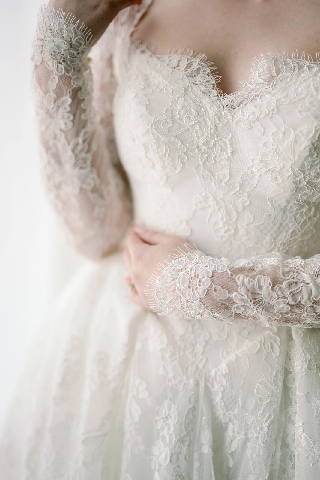Close-up of a bride in a white lace wedding dress with long sleeves and intricate lace detail.