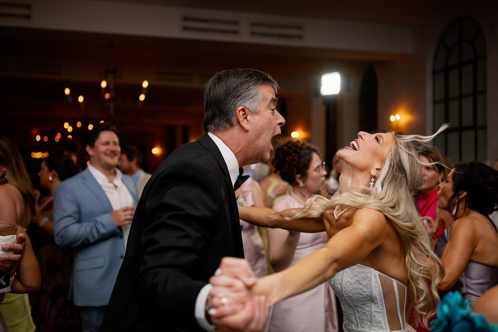 A joyful woman and an older man dancing passionately at a wedding reception, surrounded by other guests in formal attire.