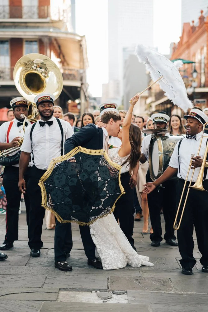Couple dancing while a marching band plays music in the background on a city street.