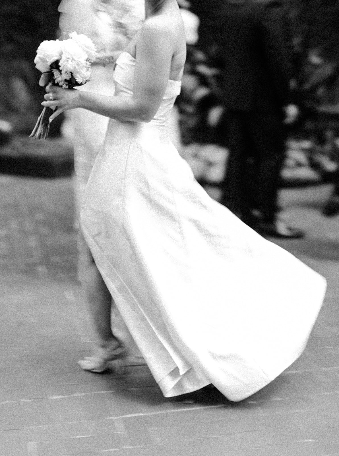 Black and white photo of a bride in a wedding gown holding a bouquet of flowers, on a dance floor.