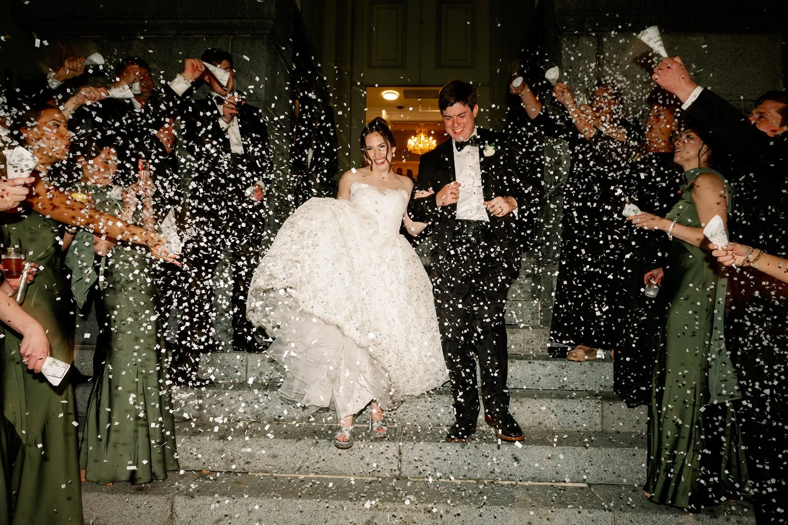 Bride and groom celebrating with confetti after wedding, walking down the steps with wedding guests throwing confetti.