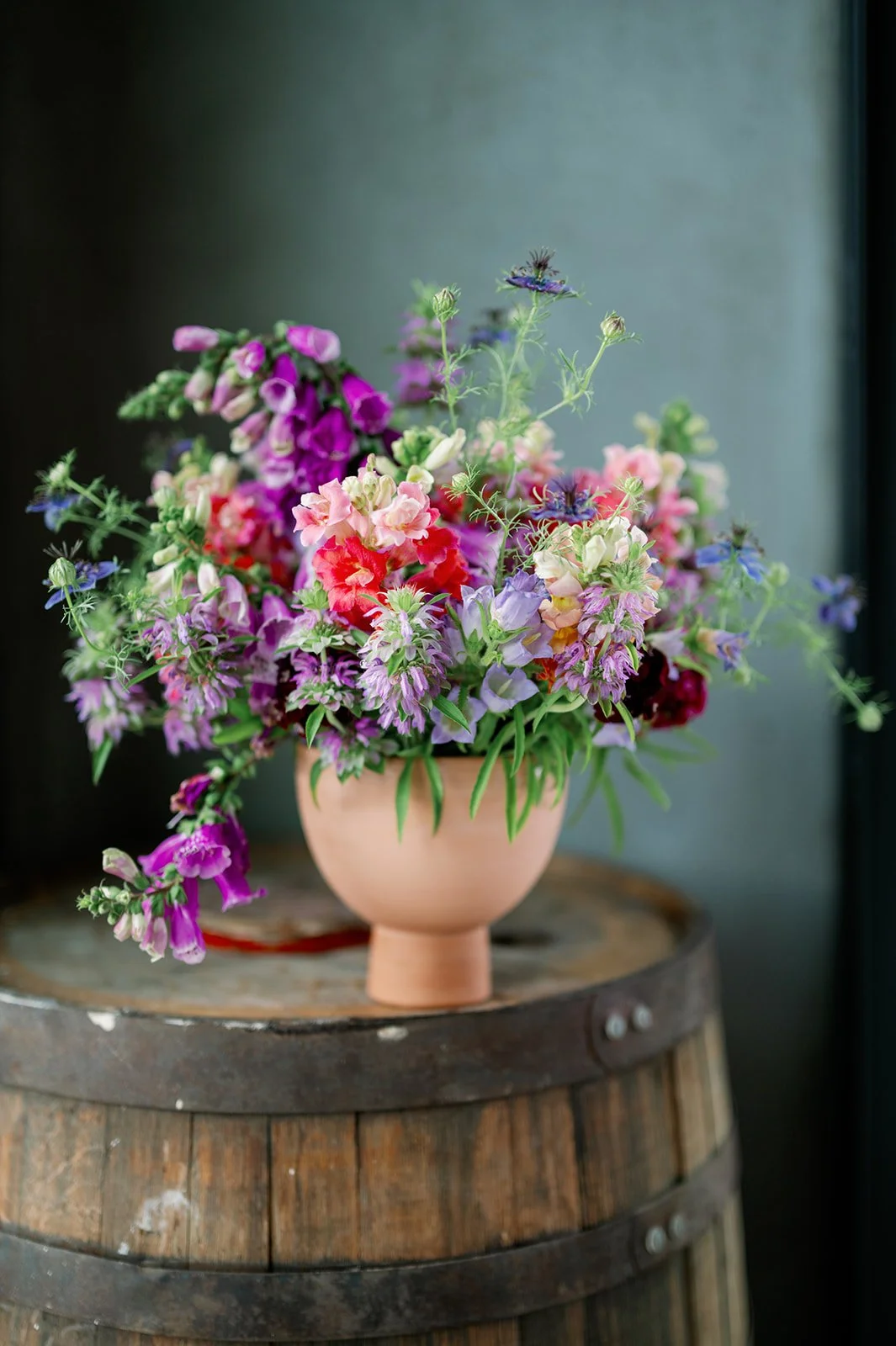 Colorful bouquet of various flowers in a pink ceramic vase on a wooden barrel.