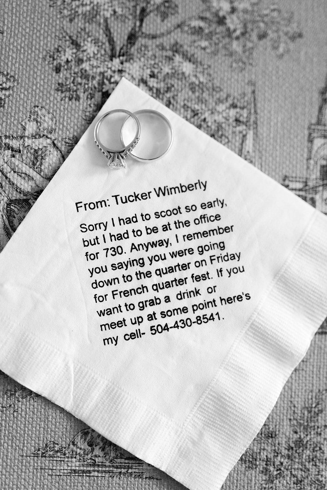 A handwritten note on a napkin with two rings placed on top of it. The note mentions a person named Tucker Wimberly and discusses meeting up for drinks or at a specific location, with a phone number provided.