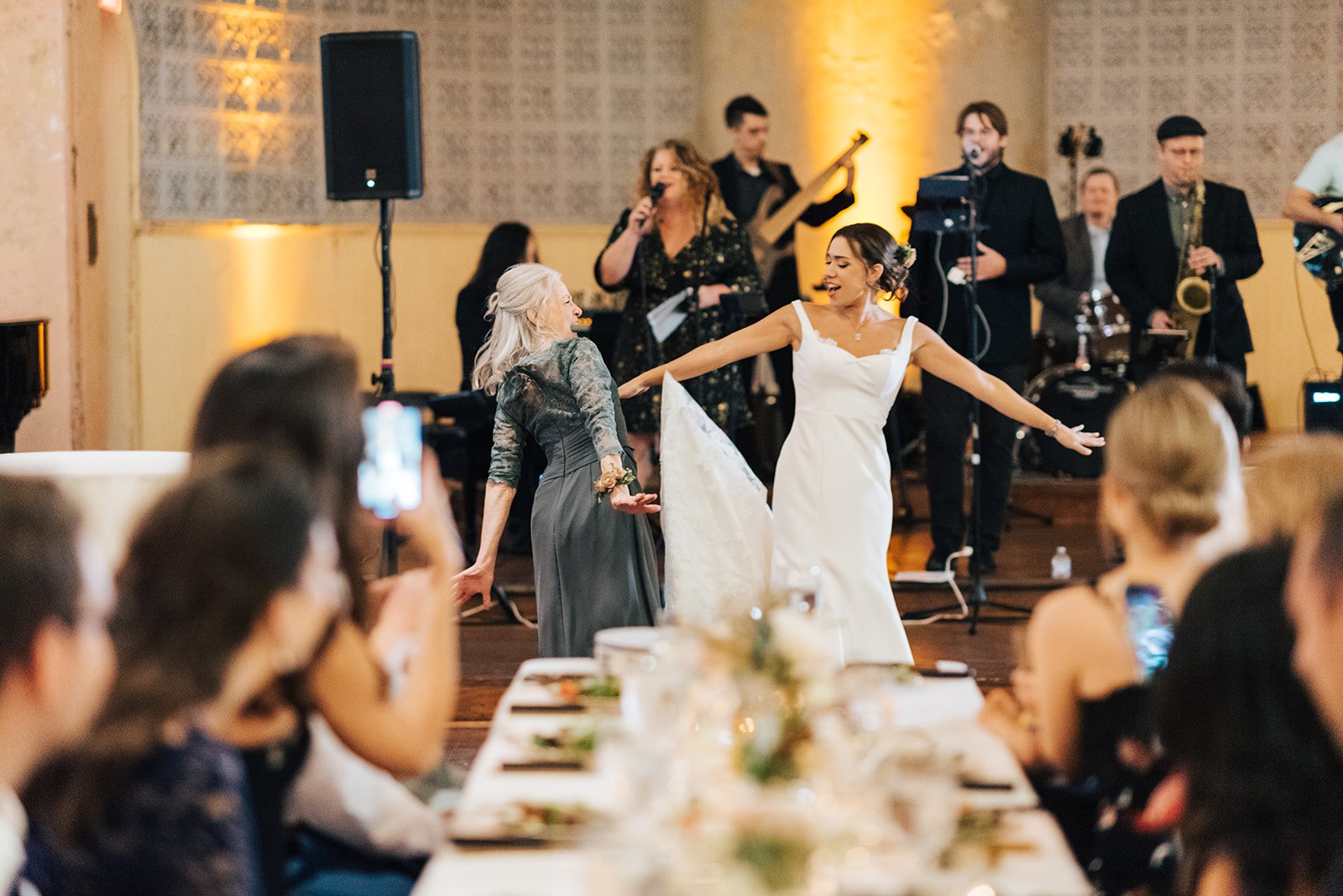 A bride dancing with an older woman at her wedding reception, with a band playing in the background.