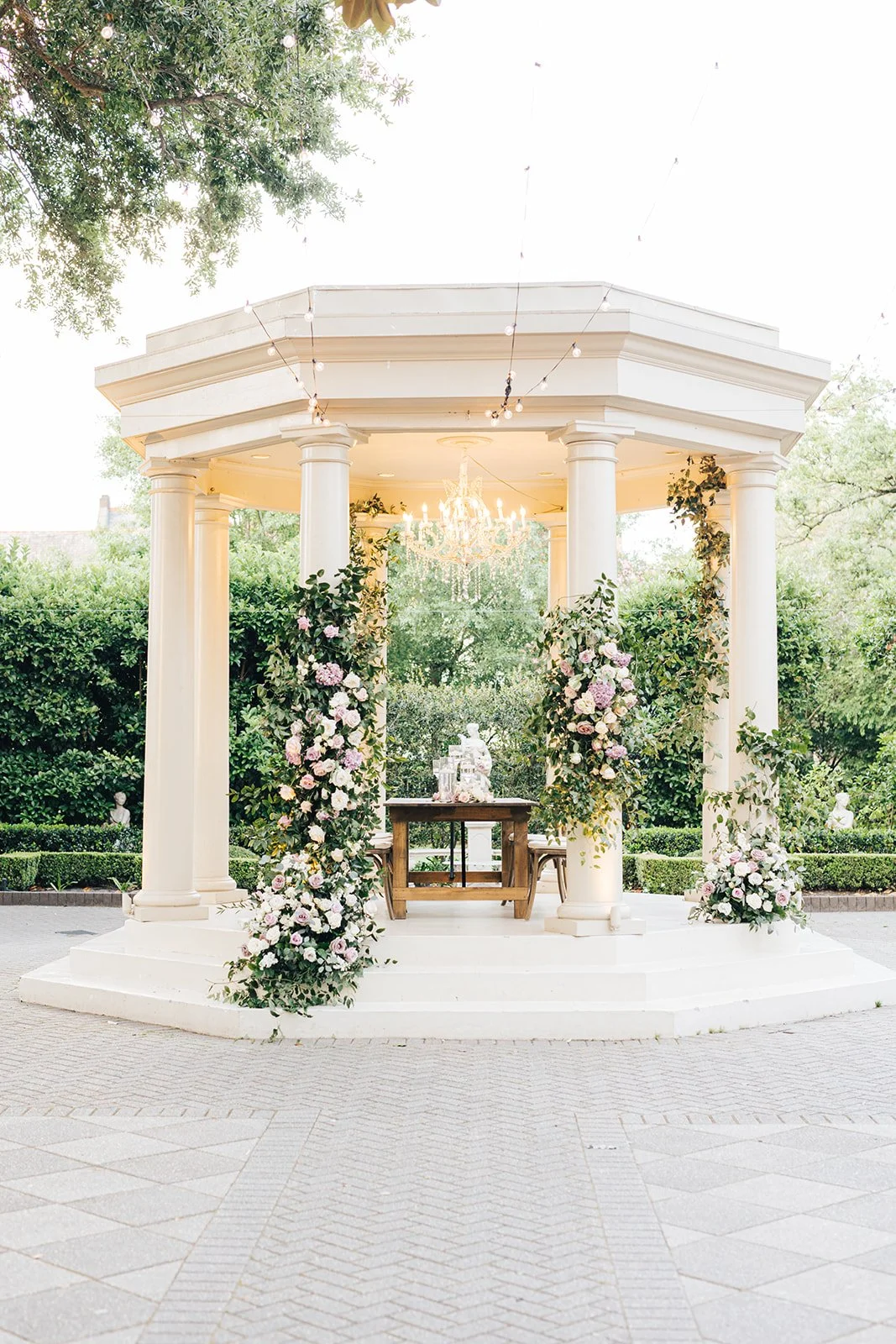 Outdoor wedding gazebo decorated with floral arrangements and a chandelier.