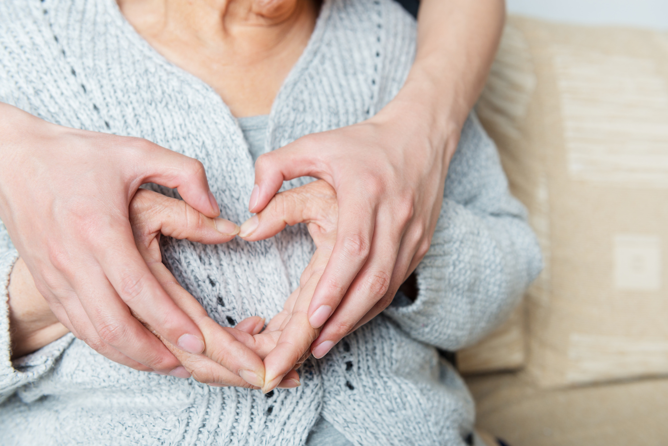 Two hands forming a heart shape over a person's chest, creating a heart outline with fingers.