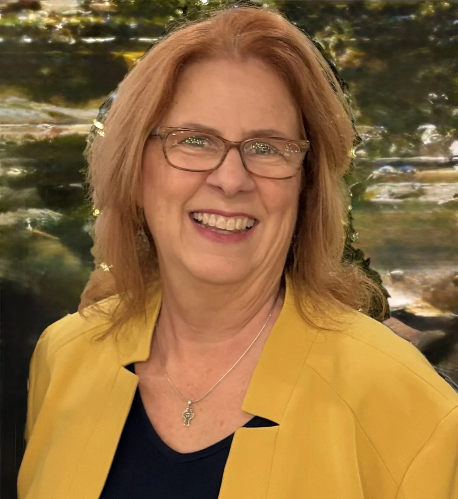 Christine, the owner of Christine's Concierge Caregiver Services. She has red hair, glasses, is wearing a yellow blazer and a black top, standing in front of a water background.