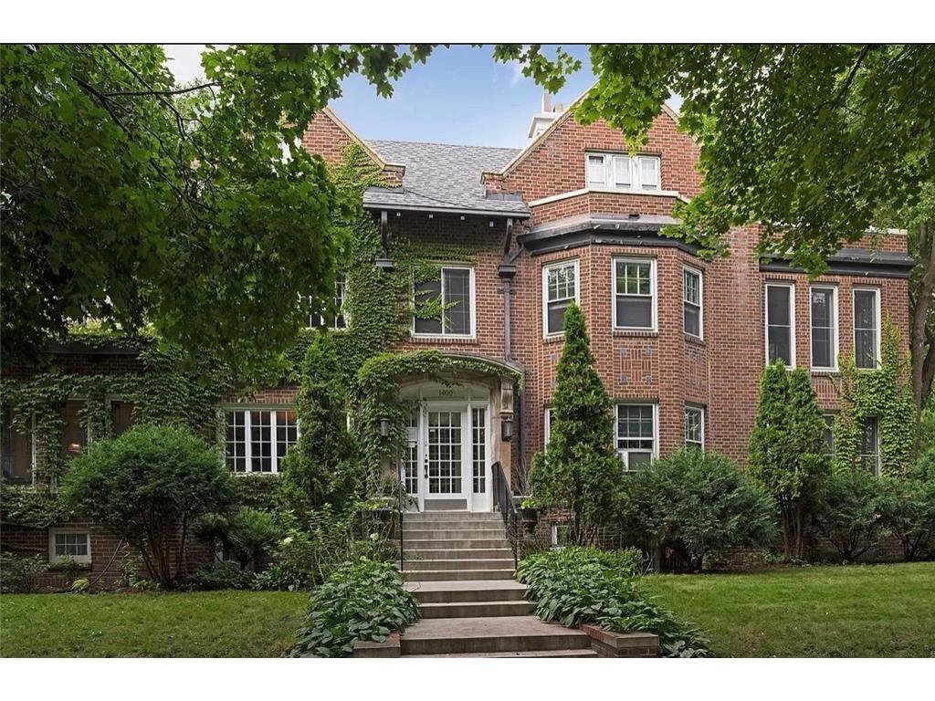 A large brick house with many windows and a front porch, surrounded by green trees and bushes. Minneapolis Luxury real estate. Nick Sundahl Realtor