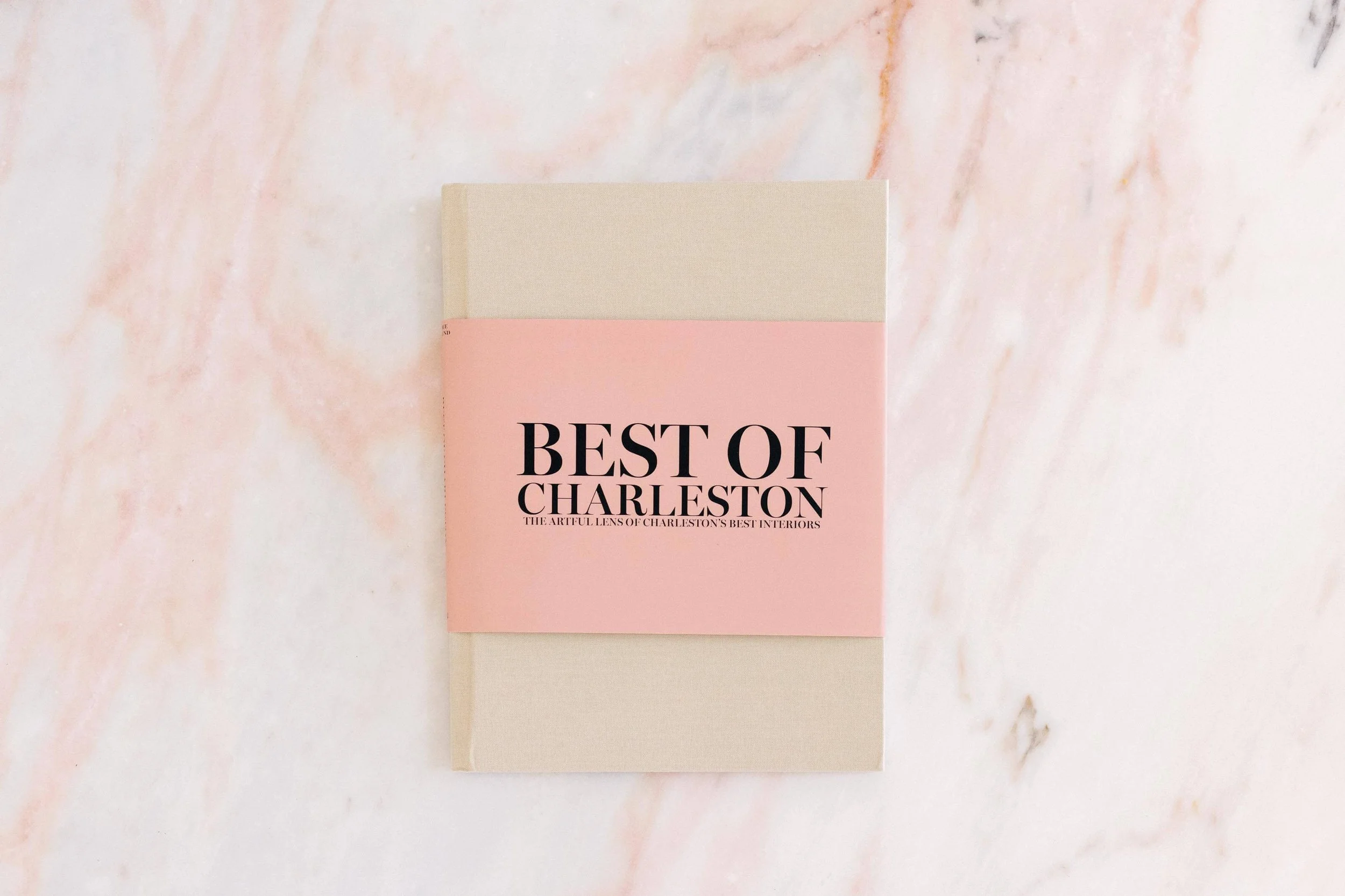A closed book with a pink cover and black text on top, placed on a light-colored, pink-tinged marble surface.