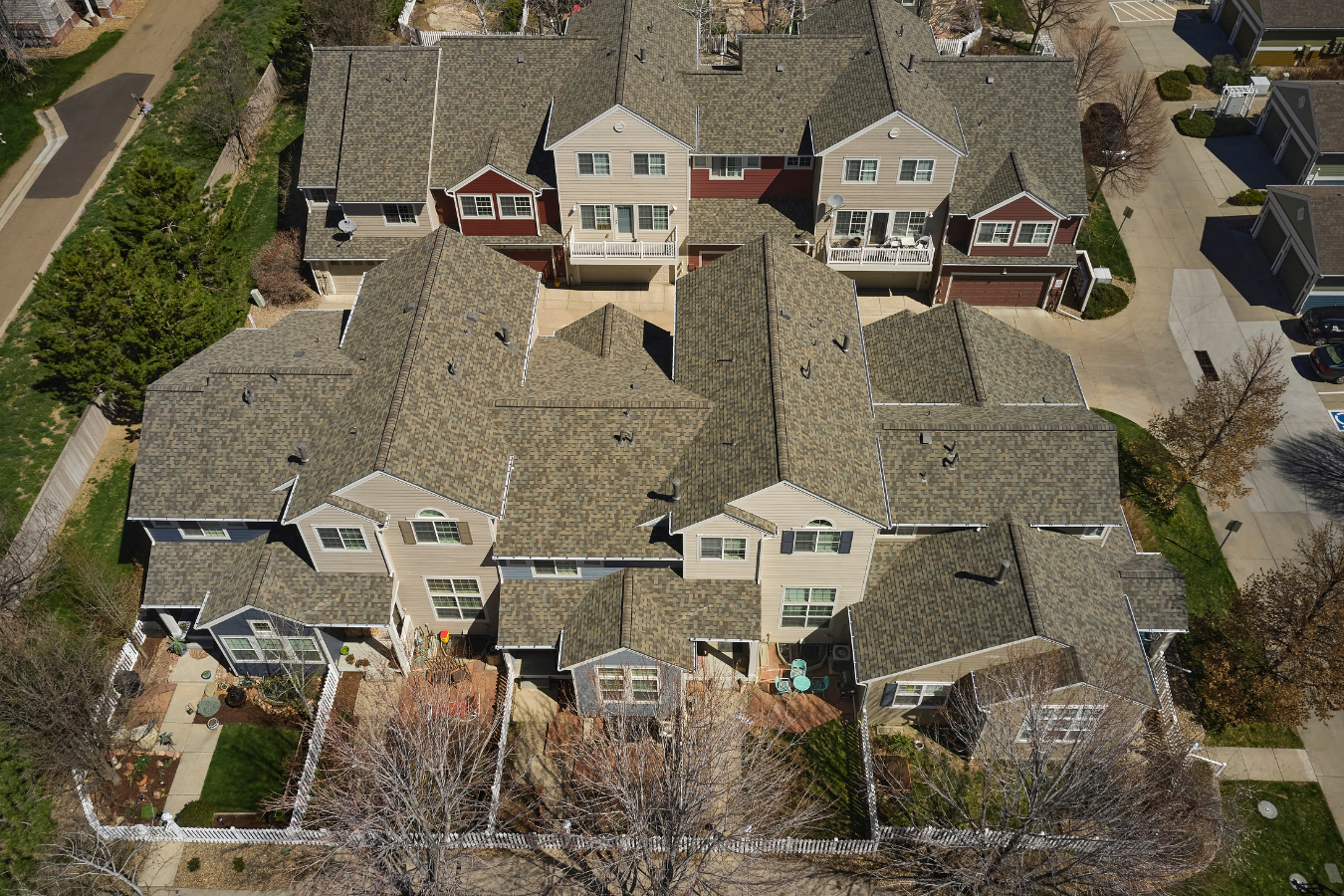 An aerial view of a multi-unit residential complex in Colorado with multiple townhouses, gray shingled roofs, and small fenced backyard patios in a suburban neighborhood.
