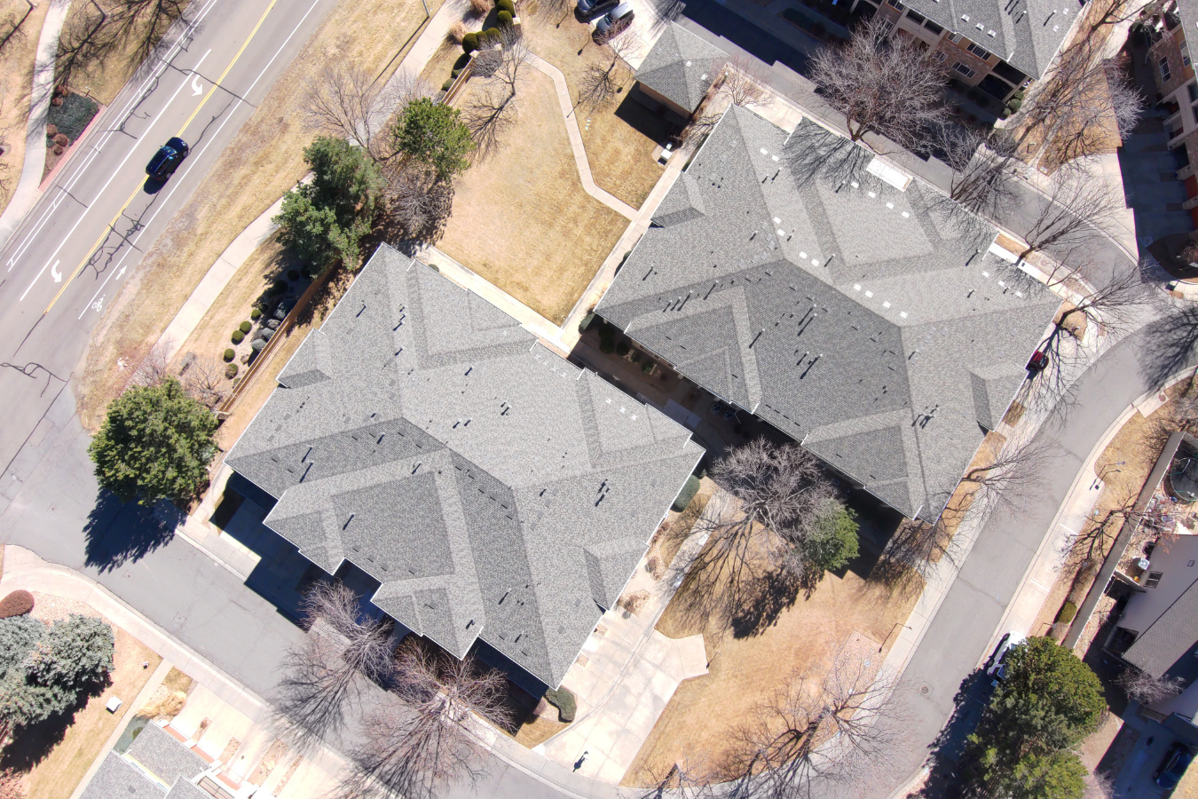 Aerial view of two large residential buildings in Colorado with gray roofs, surrounded by trees, walkways, and grassy areas in a suburban neighborhood.
