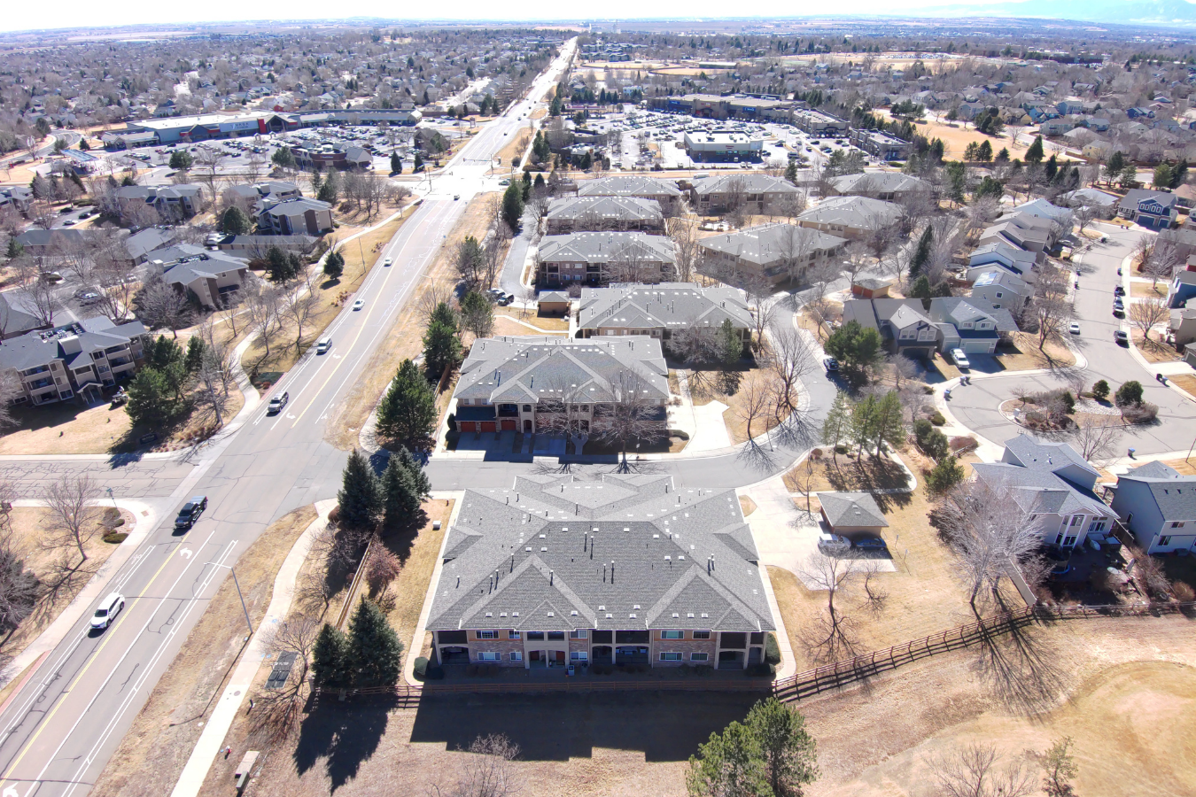 Aerial view of a suburban neighborhood in Colorado with multiple residential buildings, streets, sidewalks, trees, and parked cars, taken on a clear day.