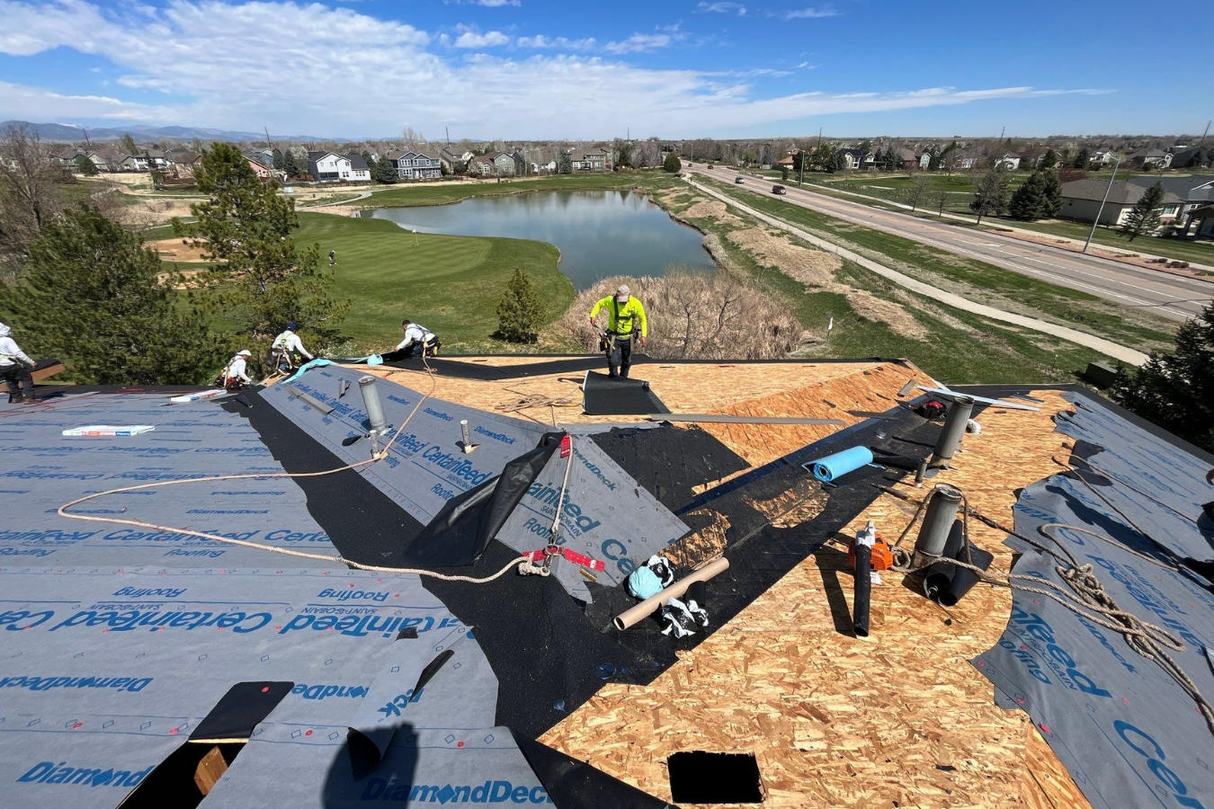 Colorado roof under construction with workers installing new roofing material, near a lake.