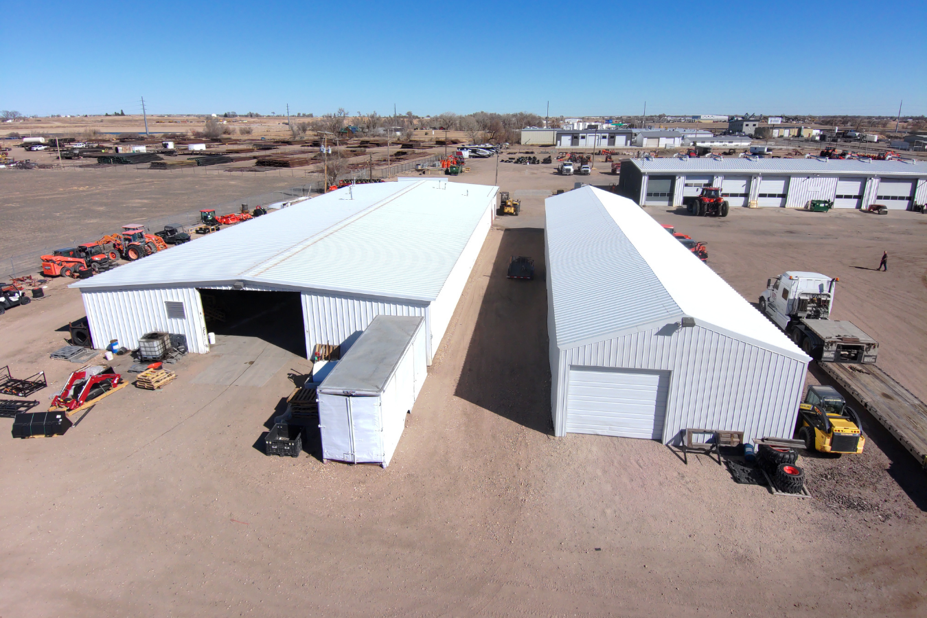 Aerial view of a commercial lot in Colorado with two large white metal buildings, surrounded by trucks, tractors, and equipment.