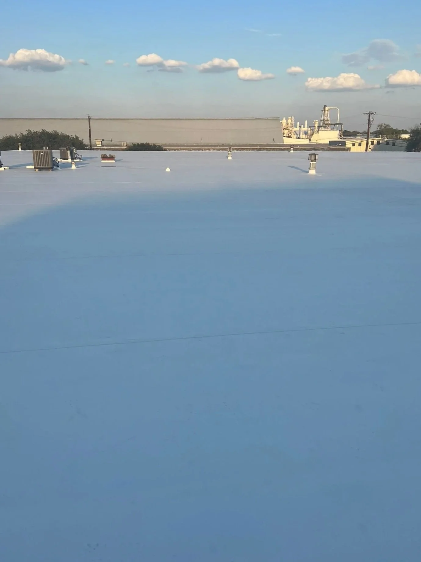 View of a flat, white rooftop under a blue sky with scattered clouds.